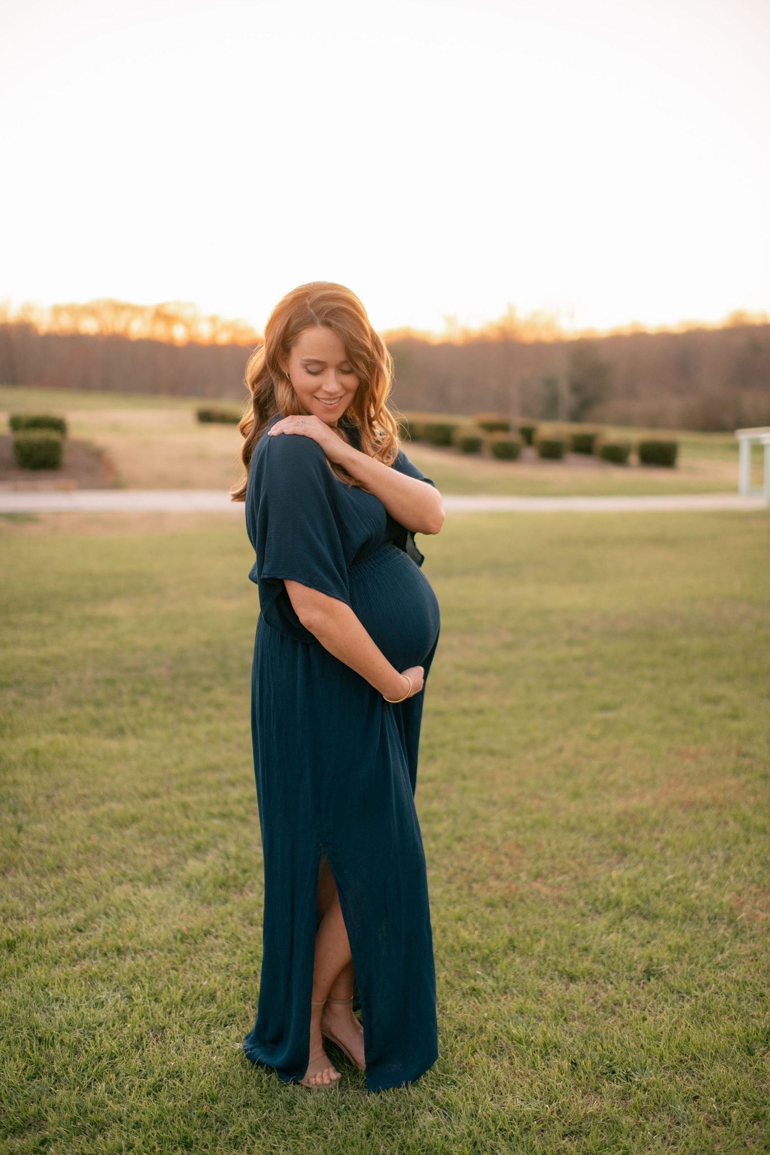 A woman in a flowing navy dress cradles her belly during a golden hour maternity photo shoot.
