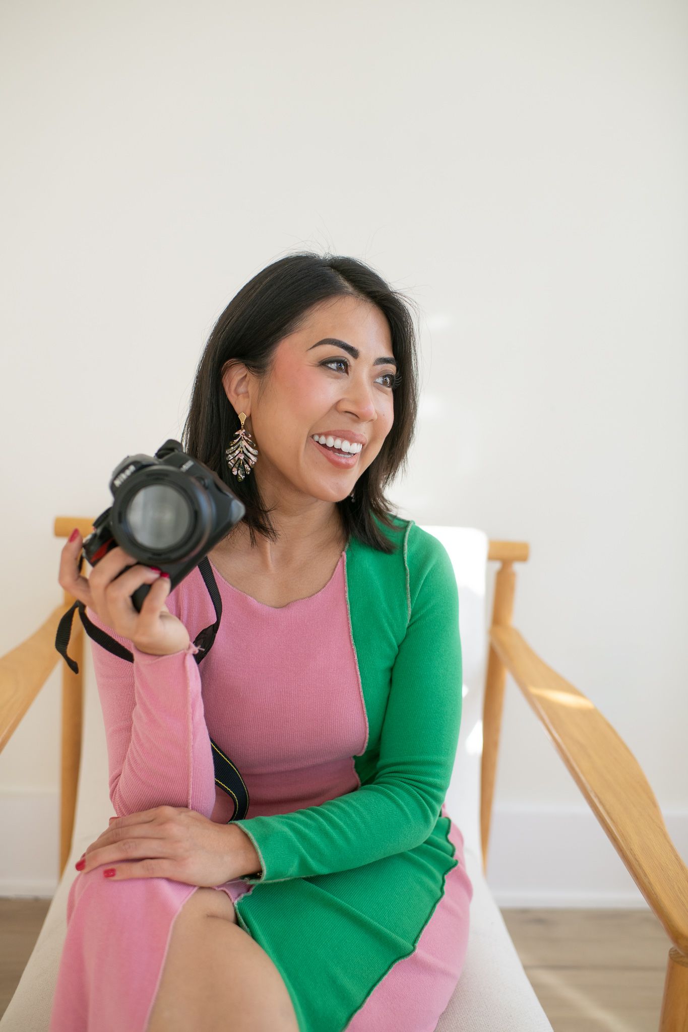 Person wearing pink and green outfit plays with headphones while sitting in wooden chair.