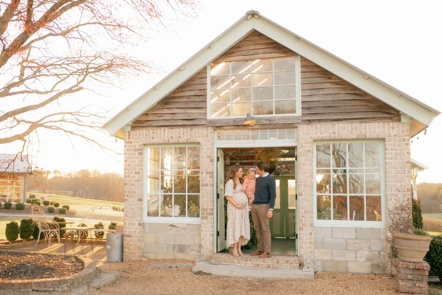 A rustic greenhouse with glass panels at sunset captures a warm glow as a pair stands in the doorway.
