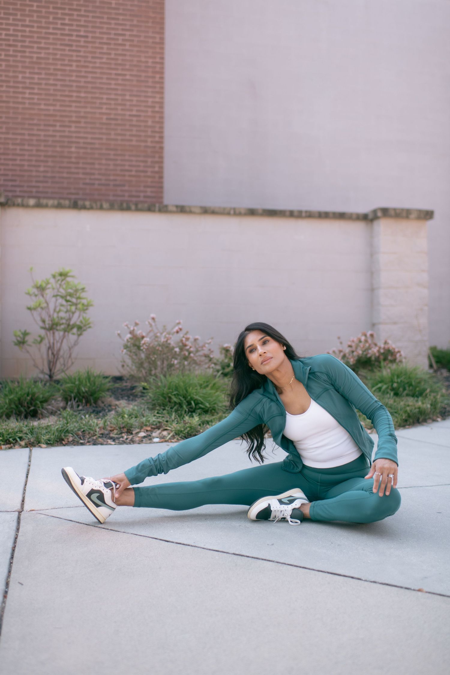 Person demonstrating stretching poses in teal athletic wear on concrete ground against white wall.