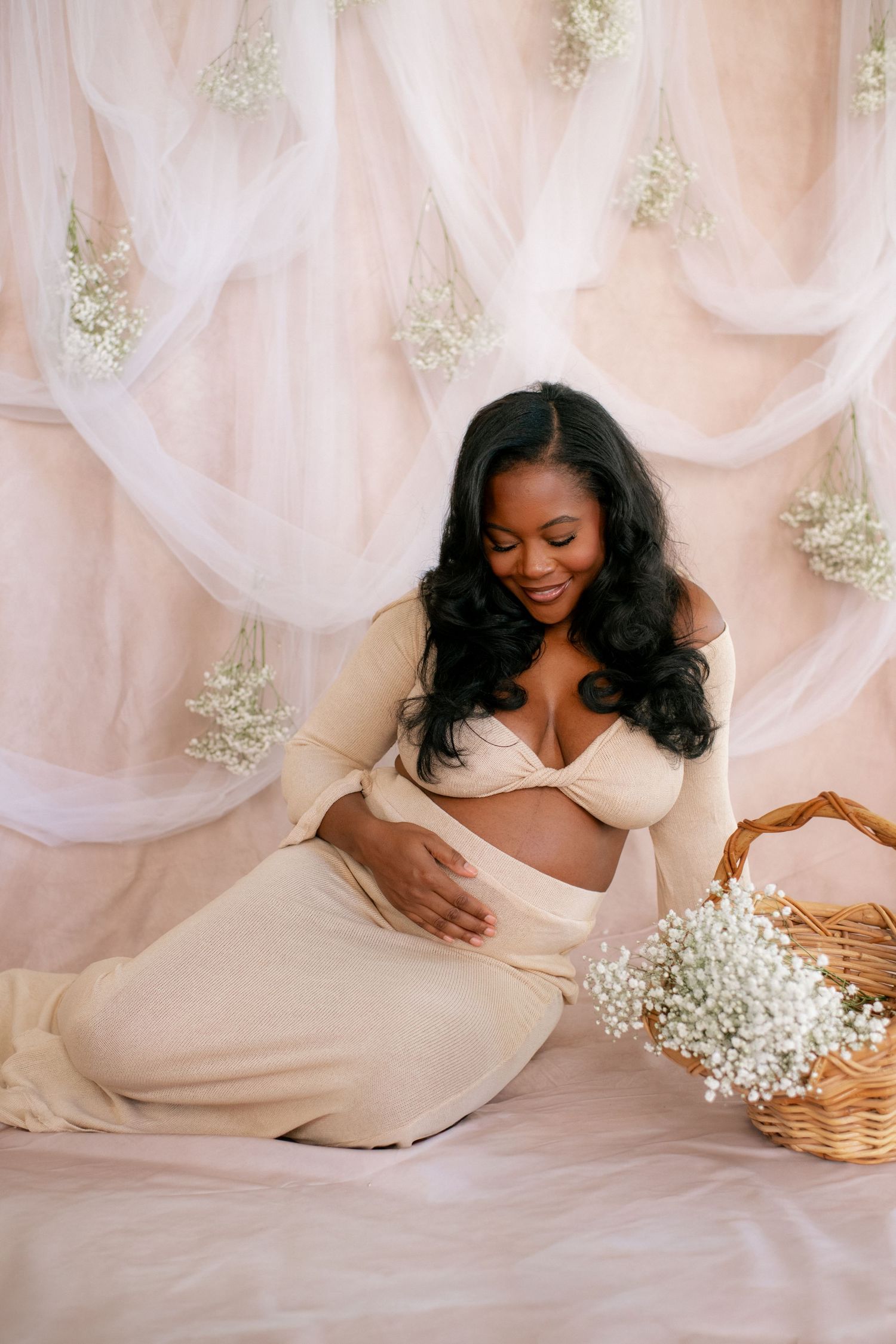 Maternity portrait with baby's breath flowers in basket against pink draped backdrop.