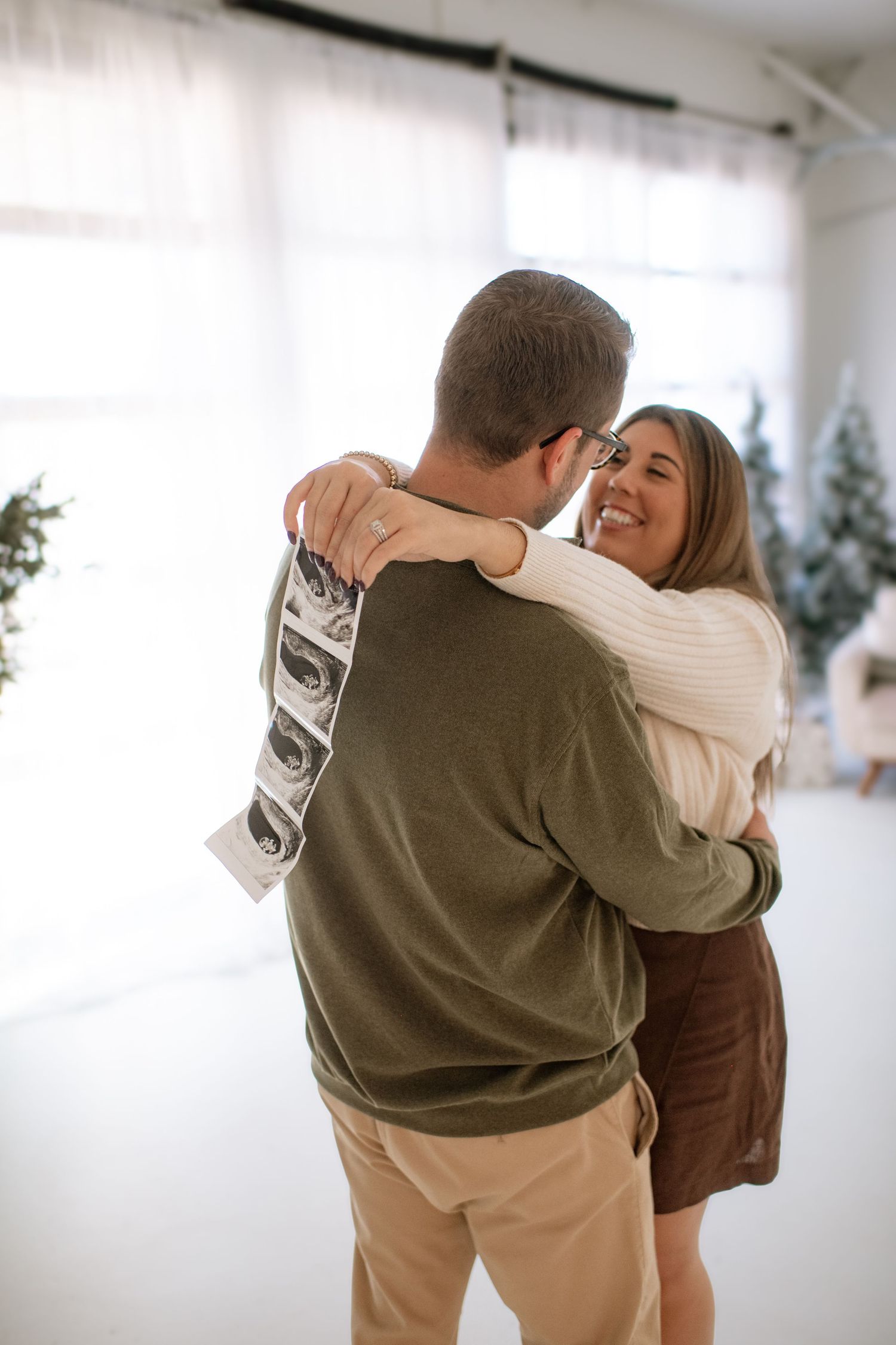 Couple in casual attire embracing in a bright indoor setting with soft lighting.