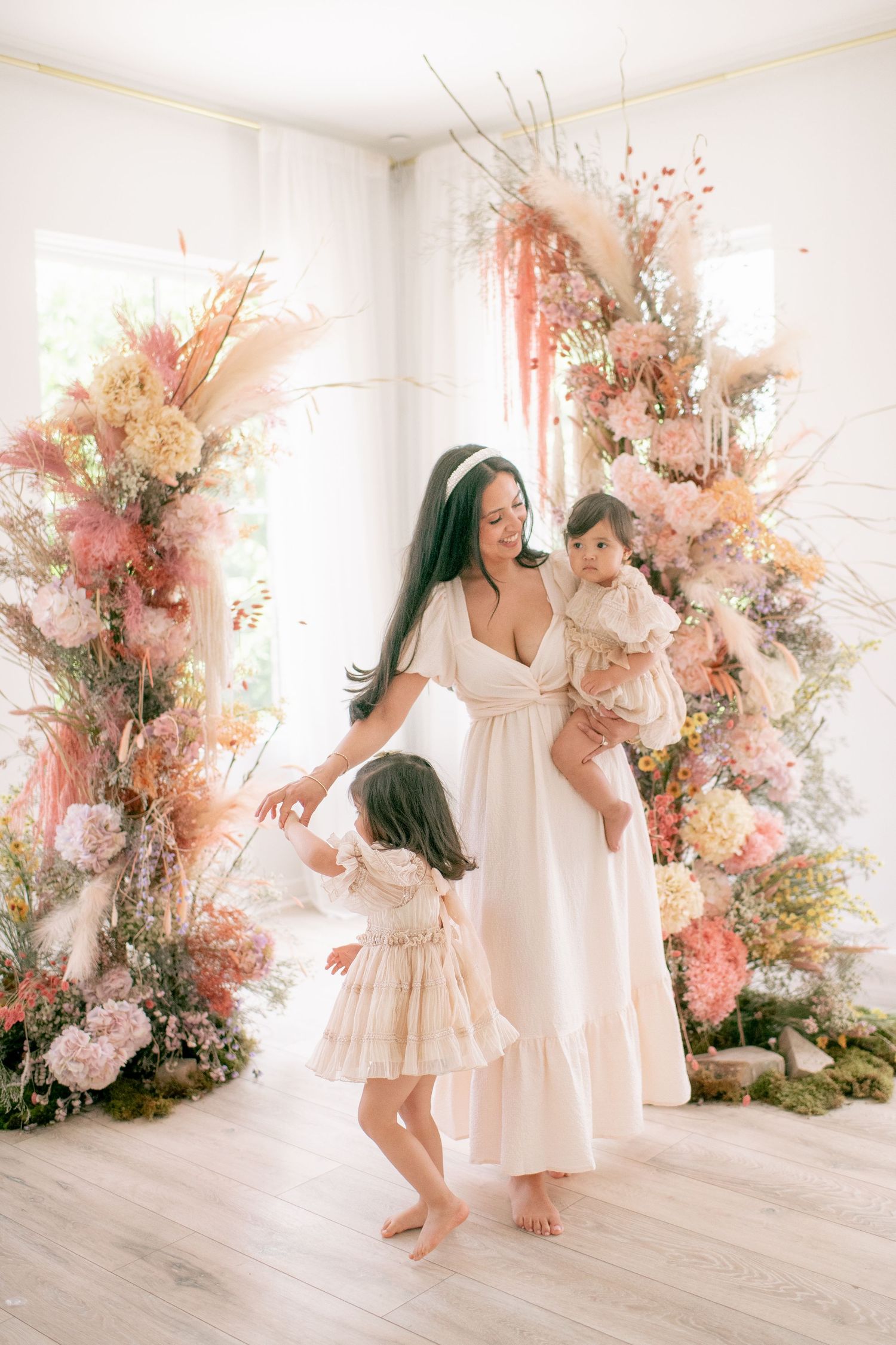 Elegant floral photoshoot scene with white dress and pink decorative arrangements in bright interior setting.