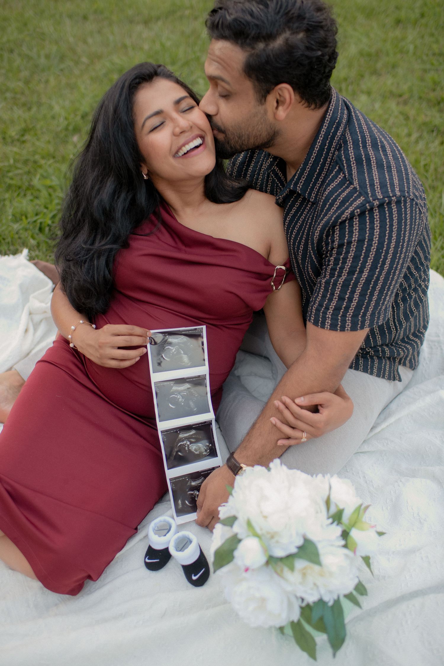 A couple shares joyful moments on a blanket outdoors while looking at ultrasound photos.