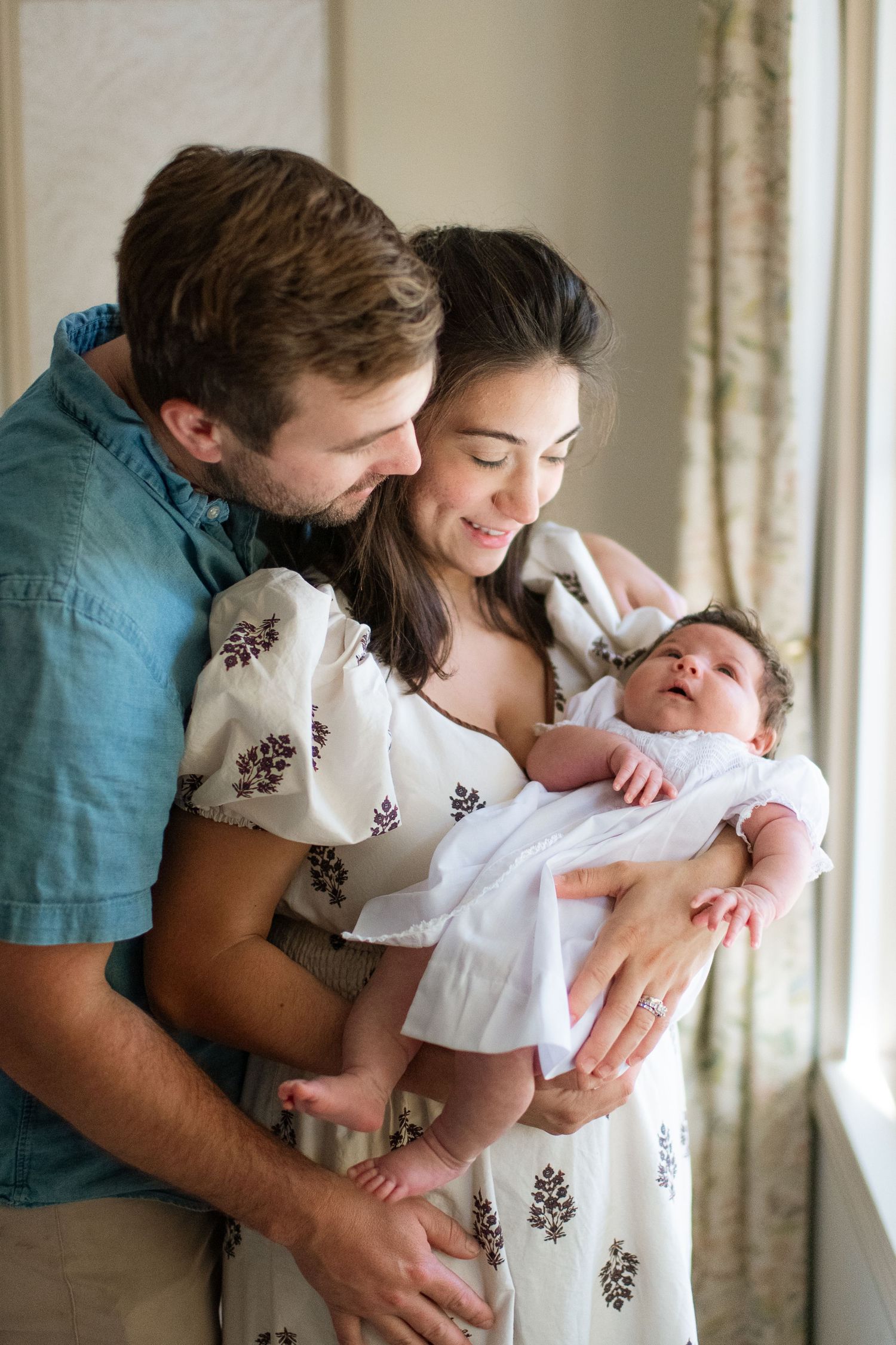 A tender moment shared with a newborn baby wearing white, captured in soft natural light.