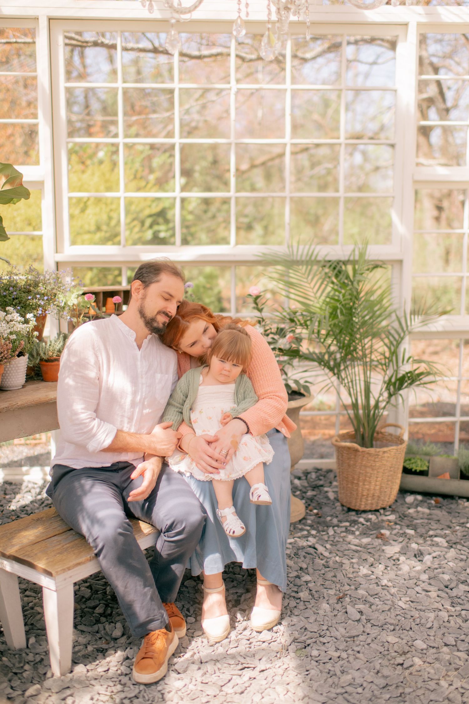 A family sits together on a rustic bench by a sunlit window with indoor plants and stone wall backdrop.