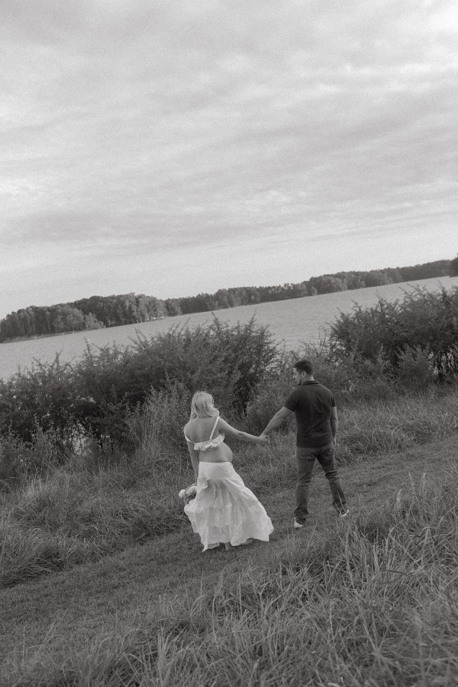 Black and white photo of couple dancing in field by water during maternity session.