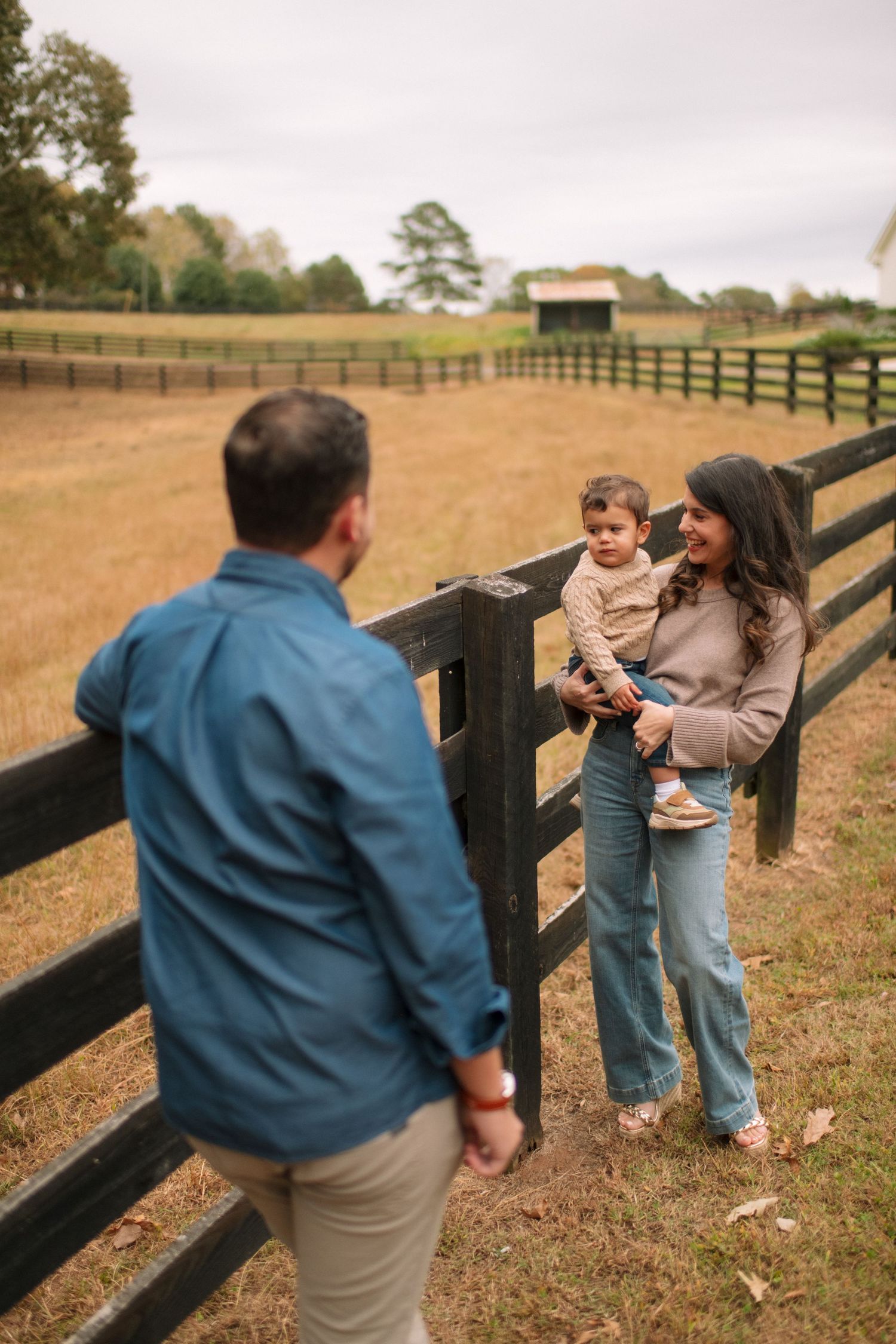 Family members share playful moments together by a wooden fence in a grassy field on an autumn afternoon.