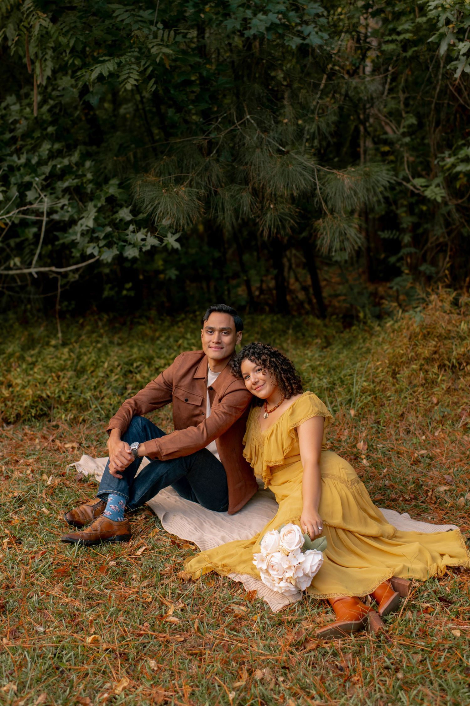 Romantic couple lounging on autumn ground with fallen leaves wearing brown and yellow outfits.