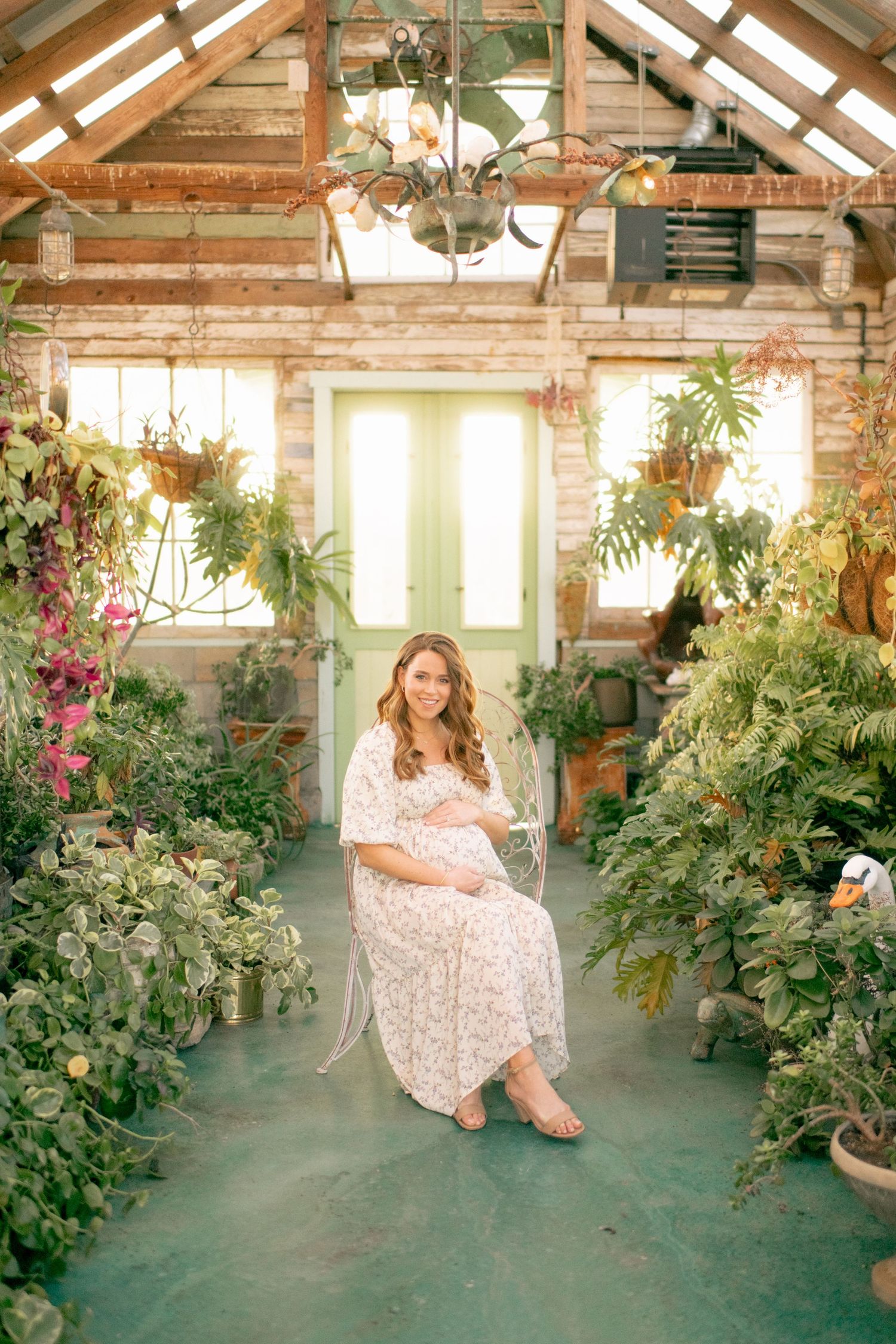 A dreamy greenhouse setting filled with lush plants and flowers surrounds a floral dress against a rustic wooden backdrop.