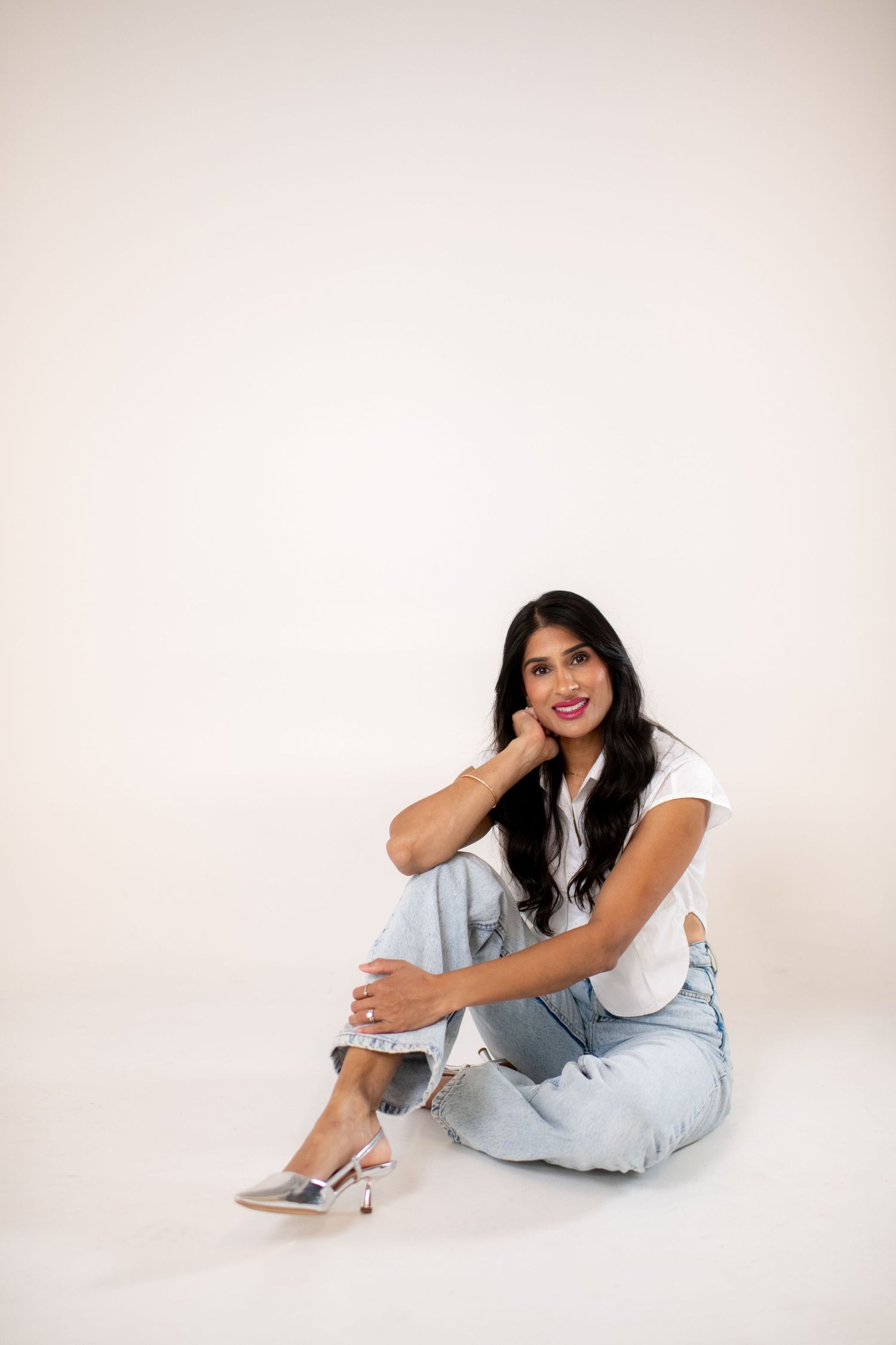 A person in casual denim and a light top poses playfully on a white studio floor in a series of lifestyle shots.
