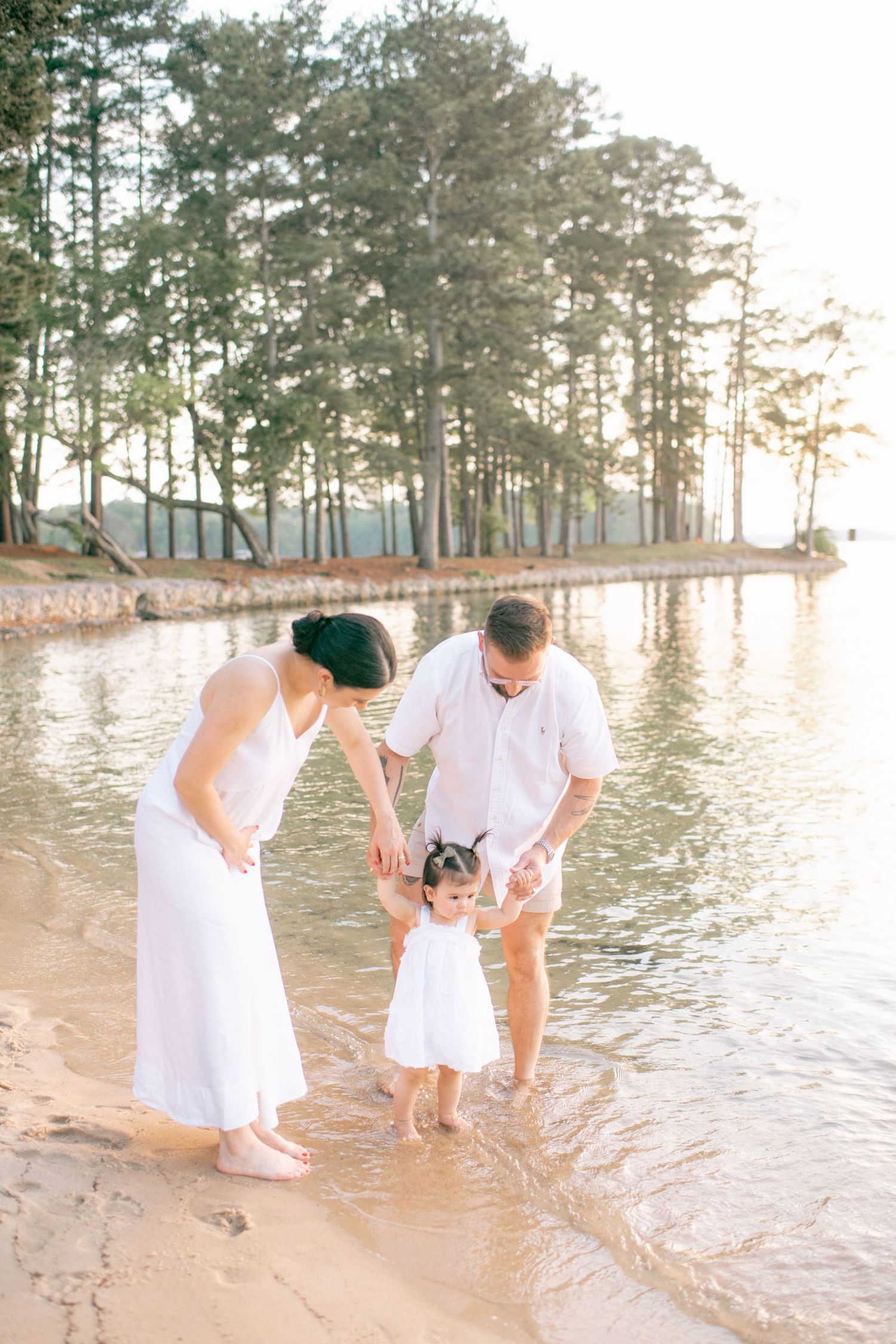 Family plays together at the water's edge during golden hour at a serene lake beach.