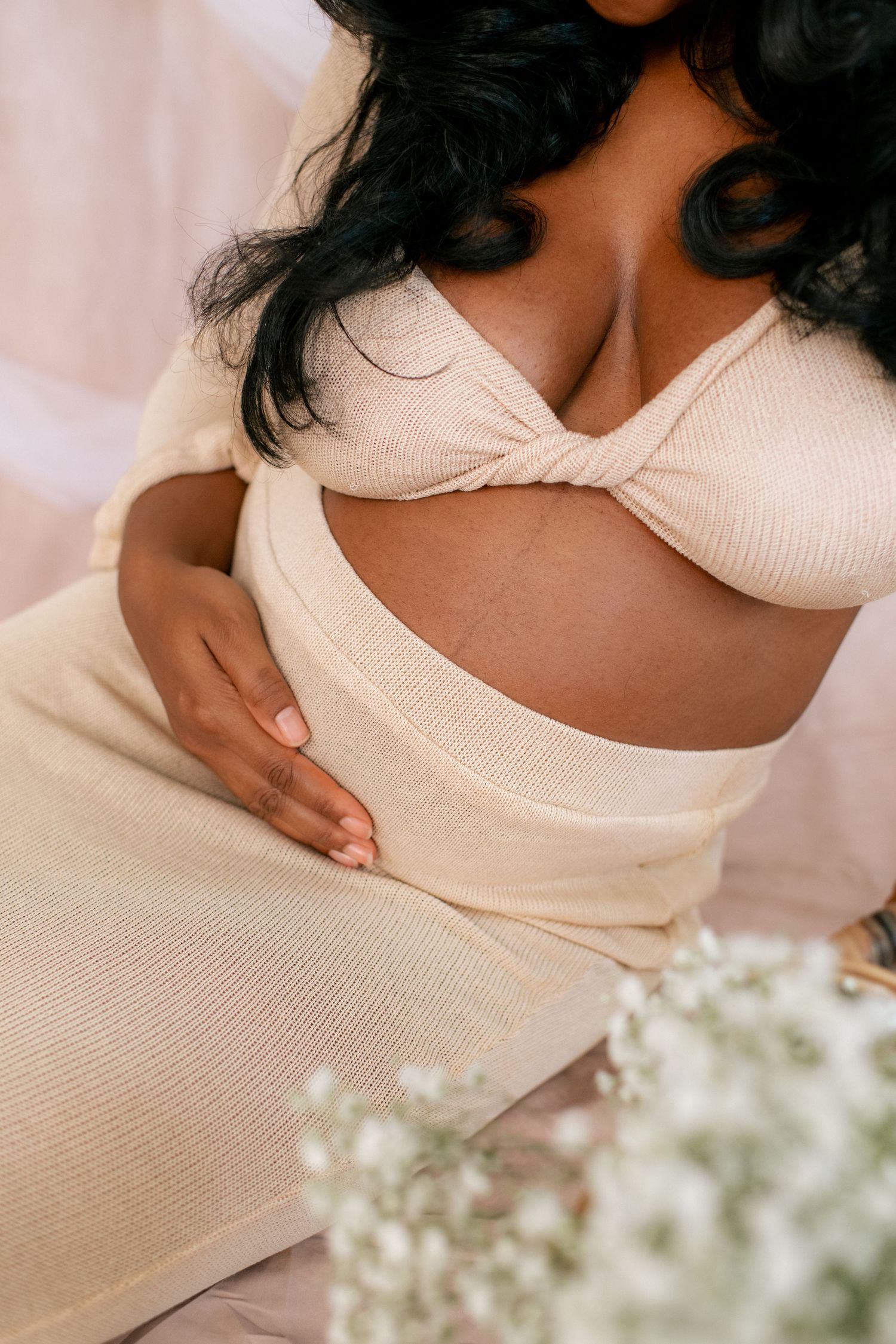 Close-up maternity photo showing cream-colored outfit details with baby's breath flowers.