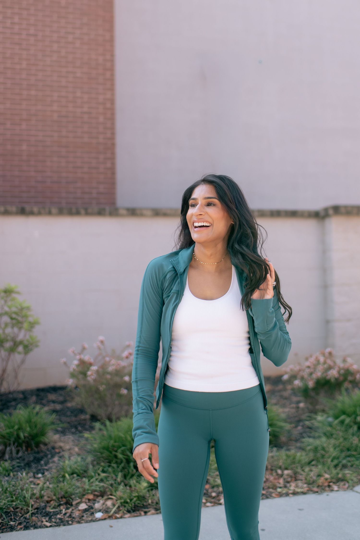 Person wearing green athletic set and white top poses against grey wall outdoors.