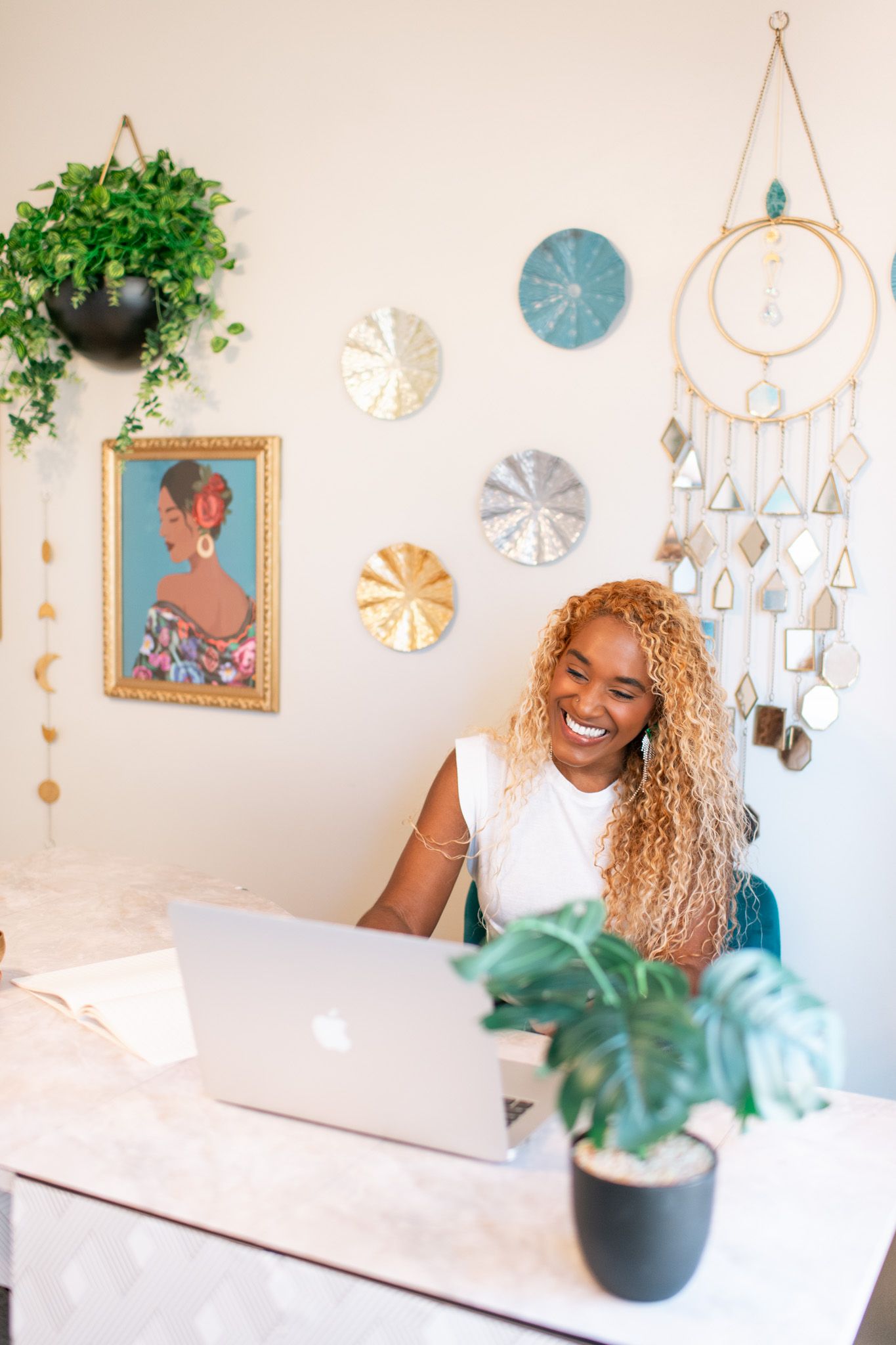 A bright and airy bedroom decorated with hanging wall art, plants, and boho-style dream catchers creates a peaceful atmosphere.