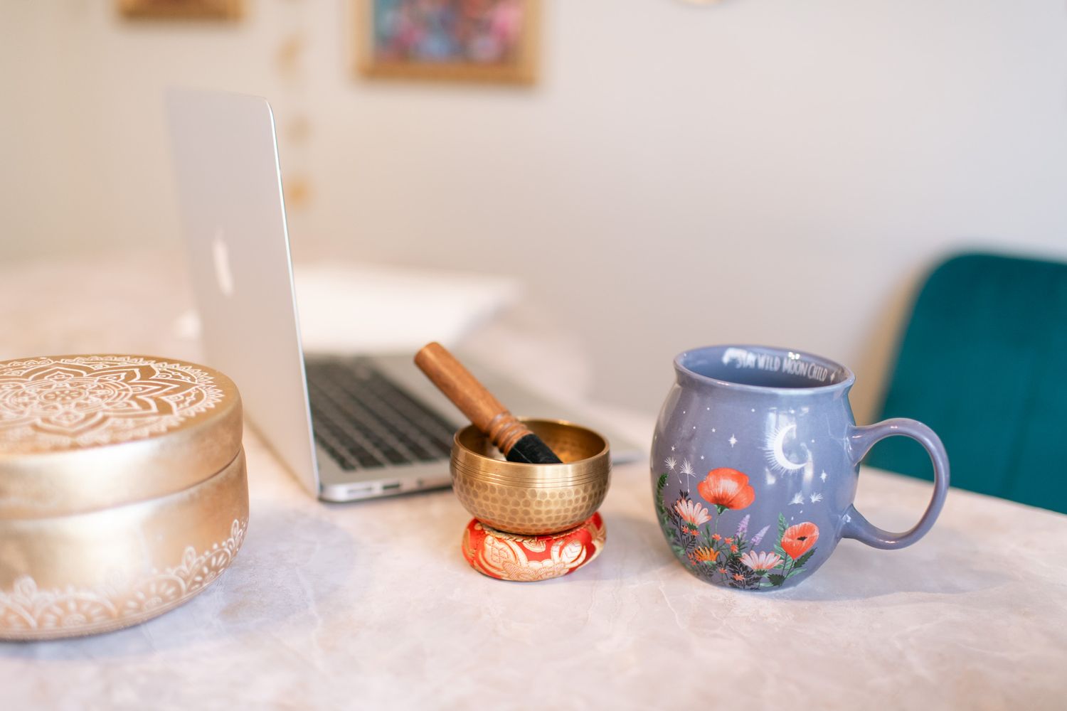 A cozy desk setup with a laptop, singing bowl, and decorative blue mug on a white marble surface.