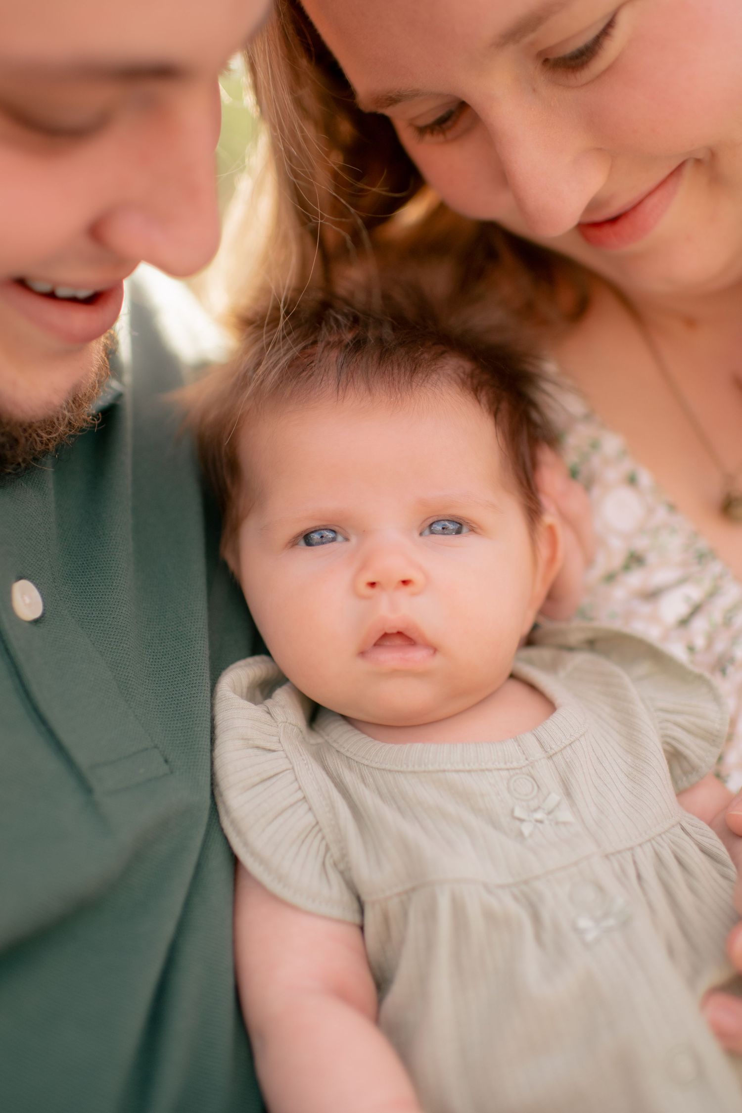 A sweet intimate family moment with a baby in a white dress between two parents.