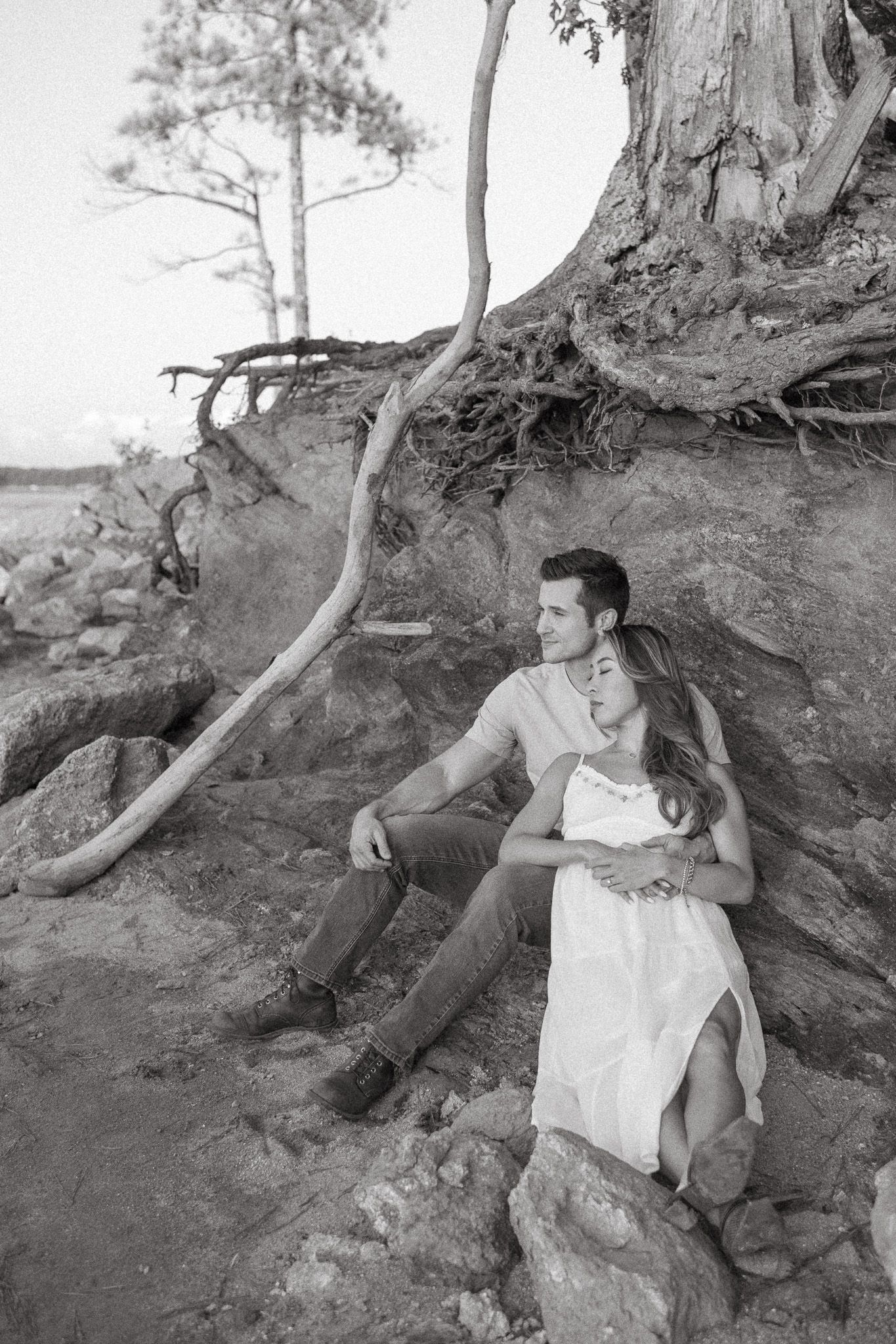 Black and white photo of a couple sitting together against exposed tree roots on a rocky hillside.