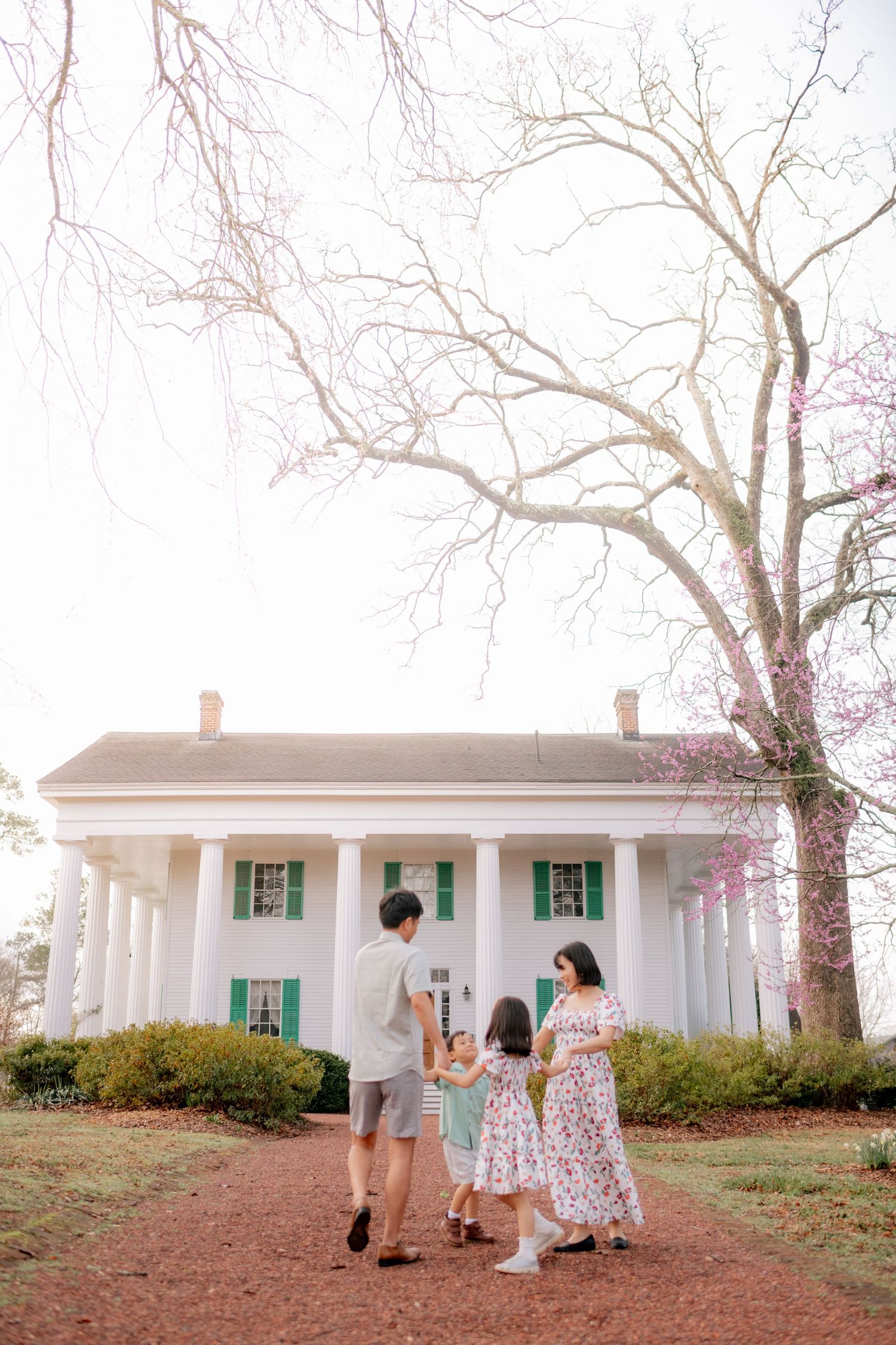 Family portrait session outside a white colonial house with columns and bare trees.