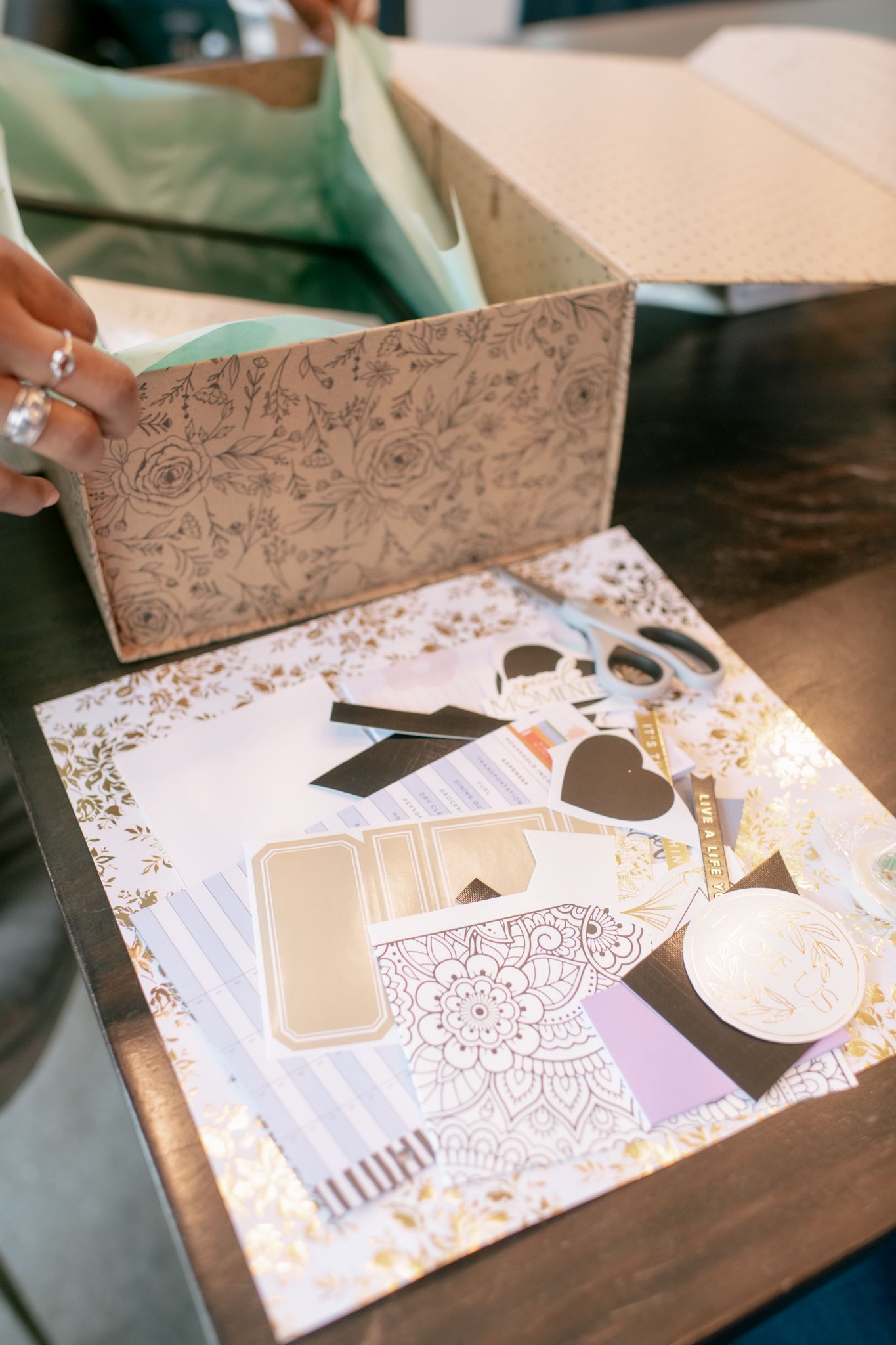 Decorative scrapbooking supplies and paper crafting elements with floral patterns and embellishments laid out on a table.