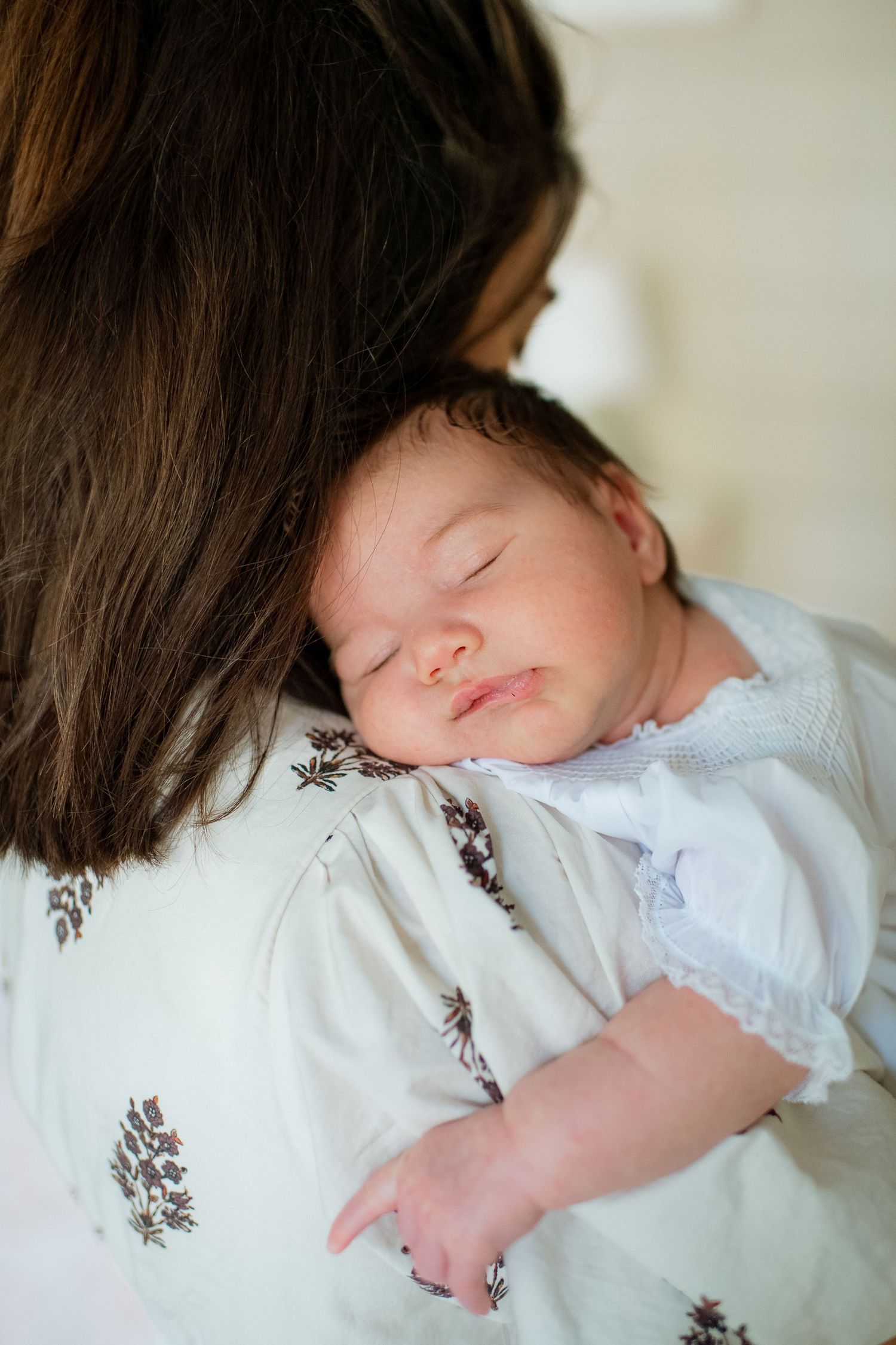 Sleeping baby in white dress with delicate embroidery details shown in a series of peaceful closeup shots.