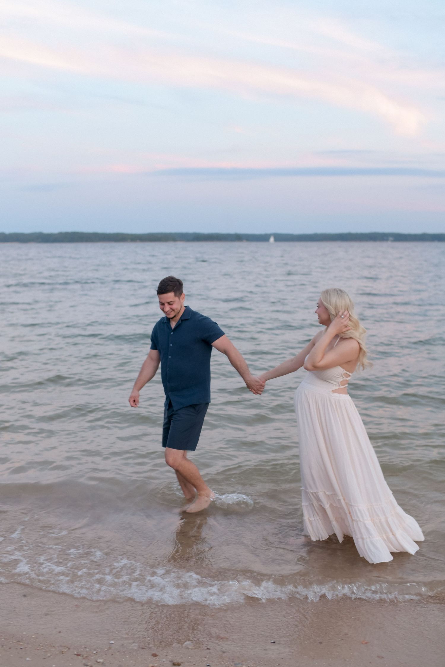 A couple splashes and plays in the shallow water during their beach maternity photoshoot.