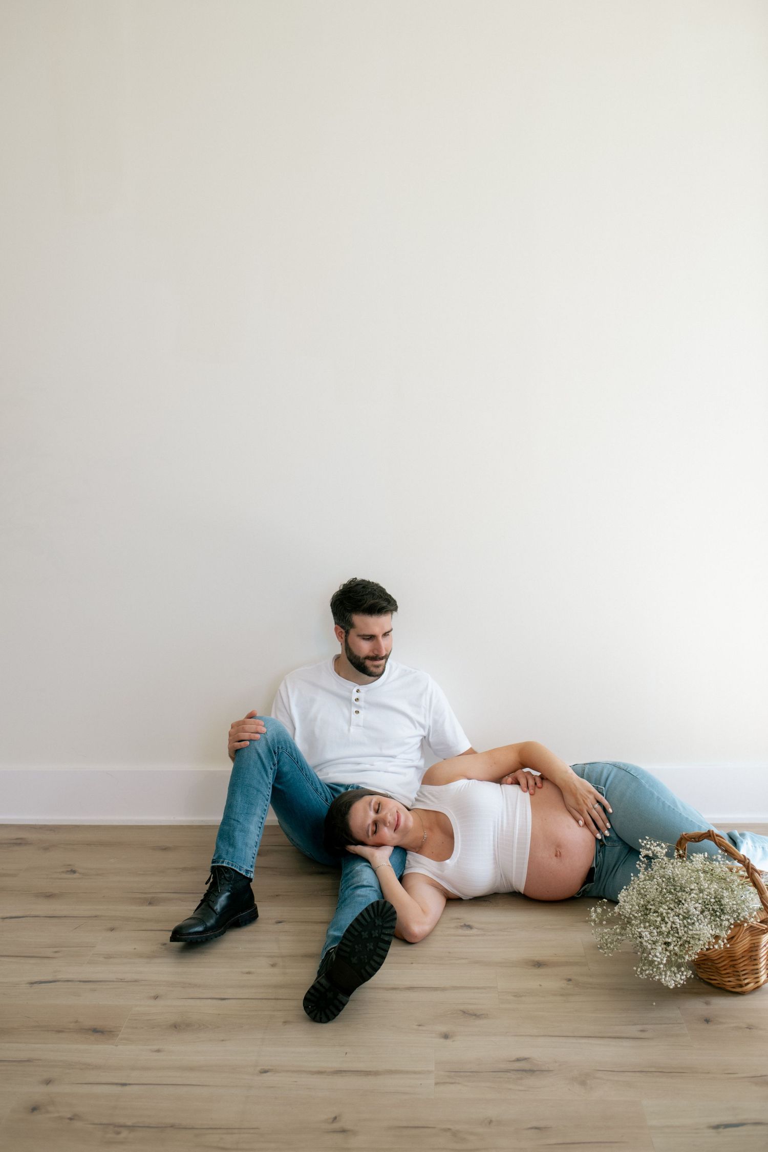 Artistic maternity photo sequence on wooden floor with natural lighting and baby's breath flowers.