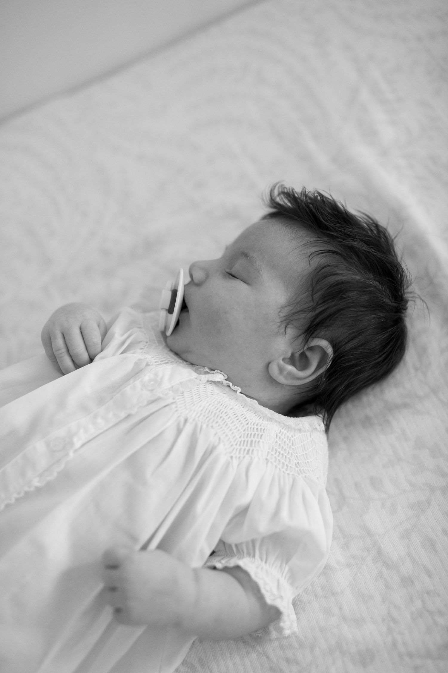 Black and white series showing a sleeping newborn in delicate white dress.