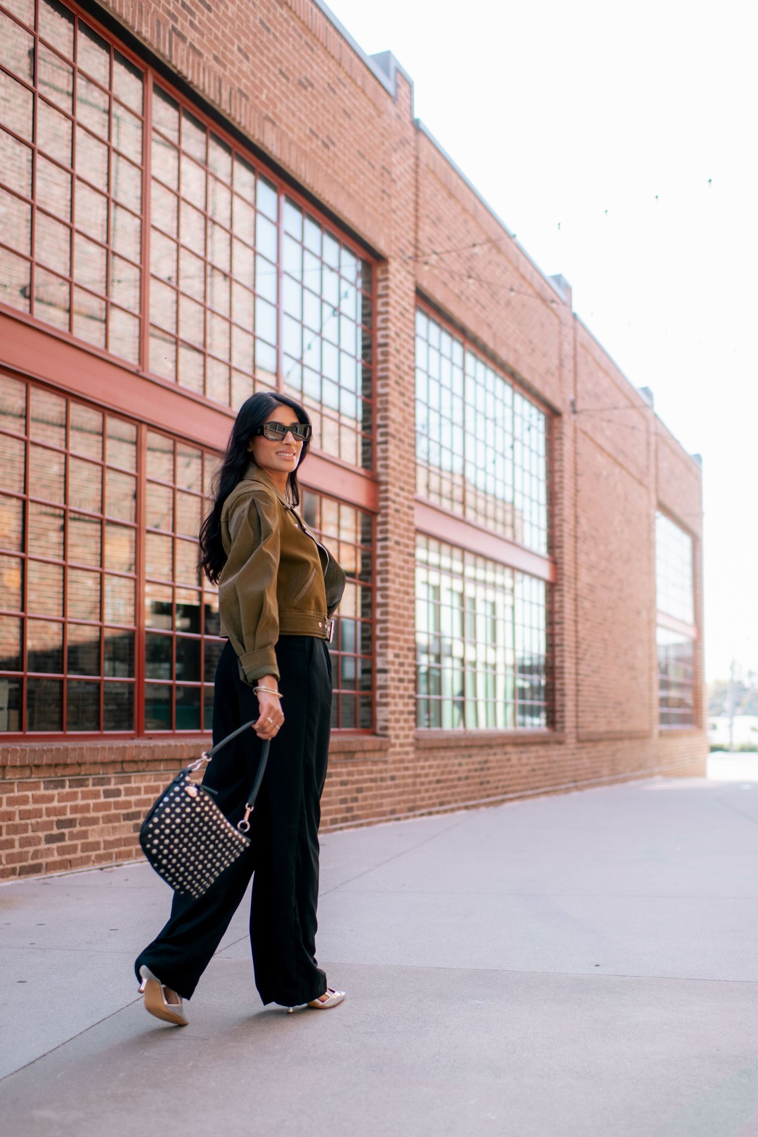 Fashion photo series showing someone walking and posing against an industrial brick building with large windows.