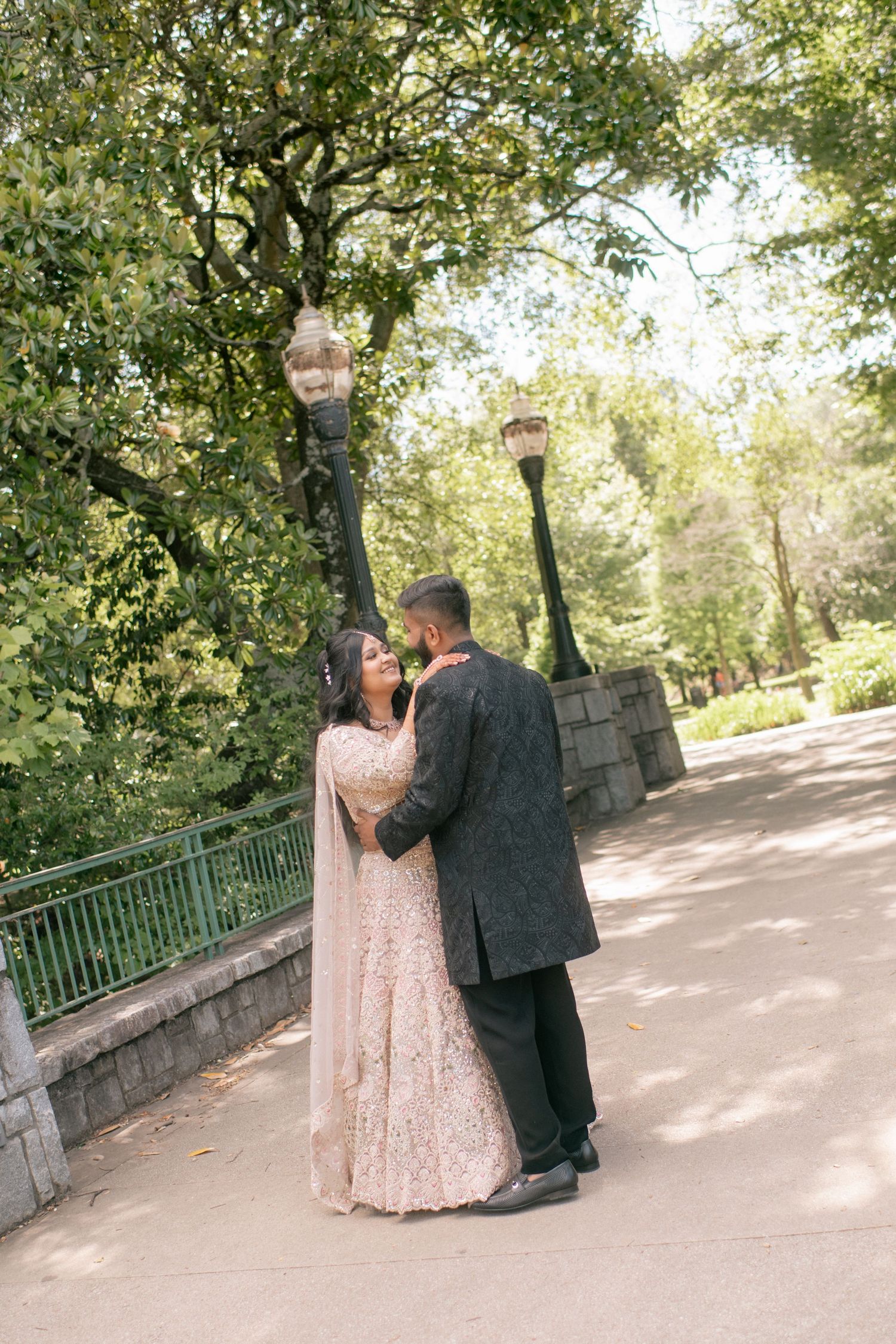 A couple shares a romantic moment on a pathway in Central Park with vintage lamp posts and lush greenery.
