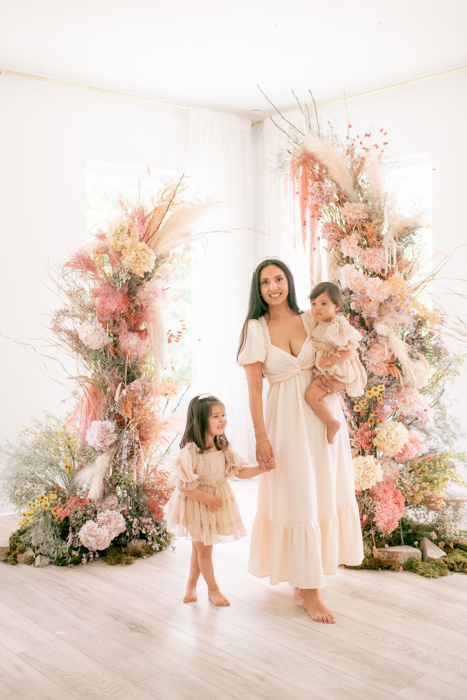 A dreamy family portrait in front of an ethereal pink and white floral arch installation in a bright minimalist space.