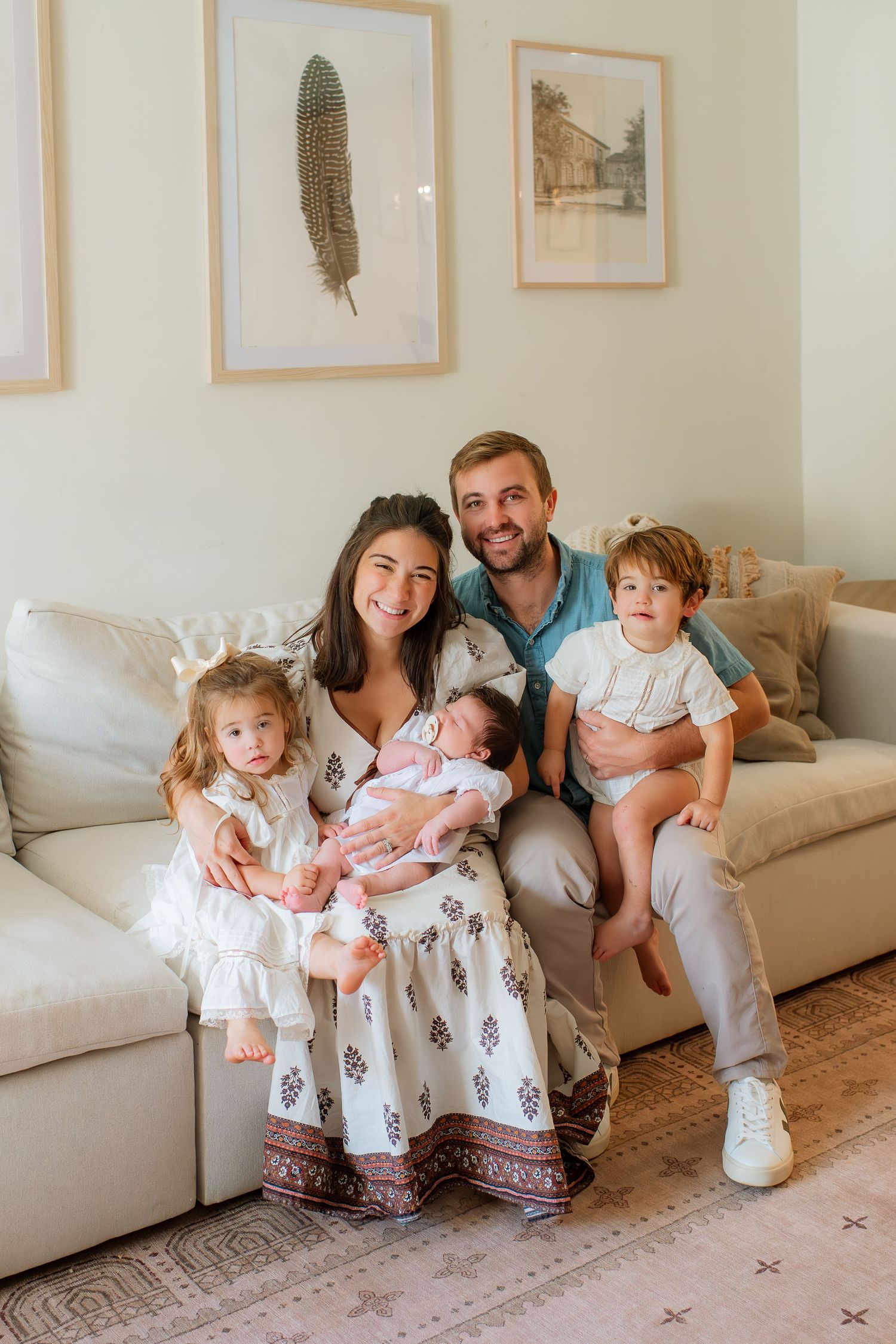 A happy family poses together on their living room couch, wearing matching white and floral outfits.