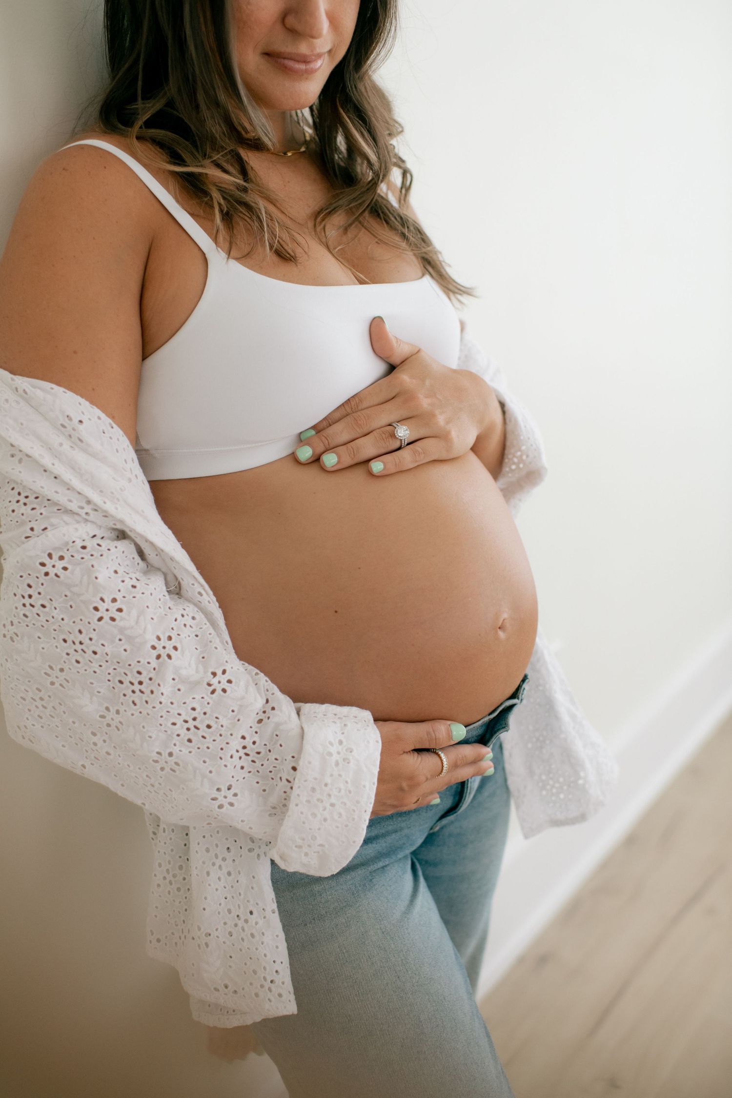 Maternity photo showing a pregnant belly with white crop top and eyelet lace cardigan.