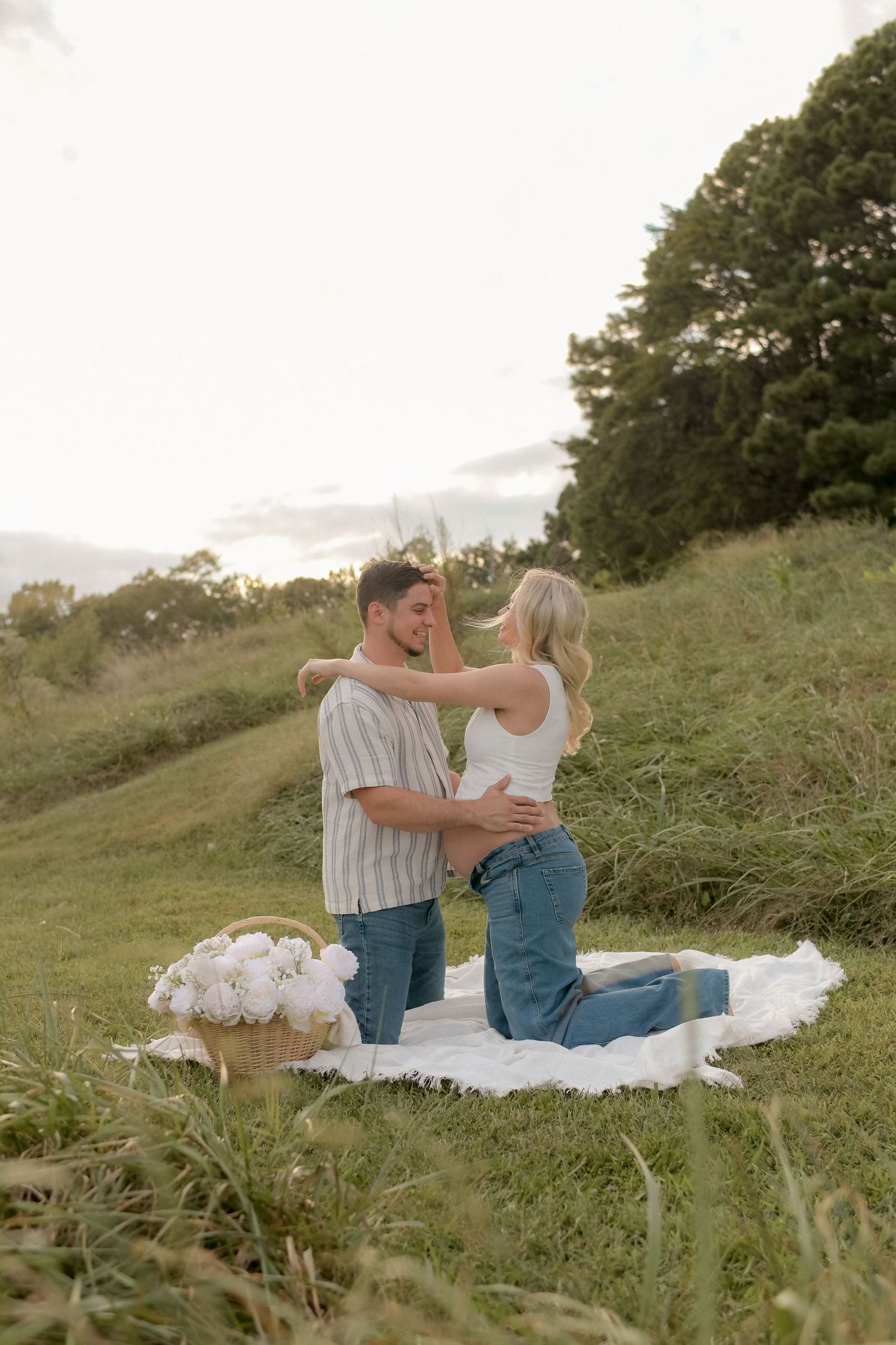 Couple sharing intimate moments on white blanket during outdoor maternity session.