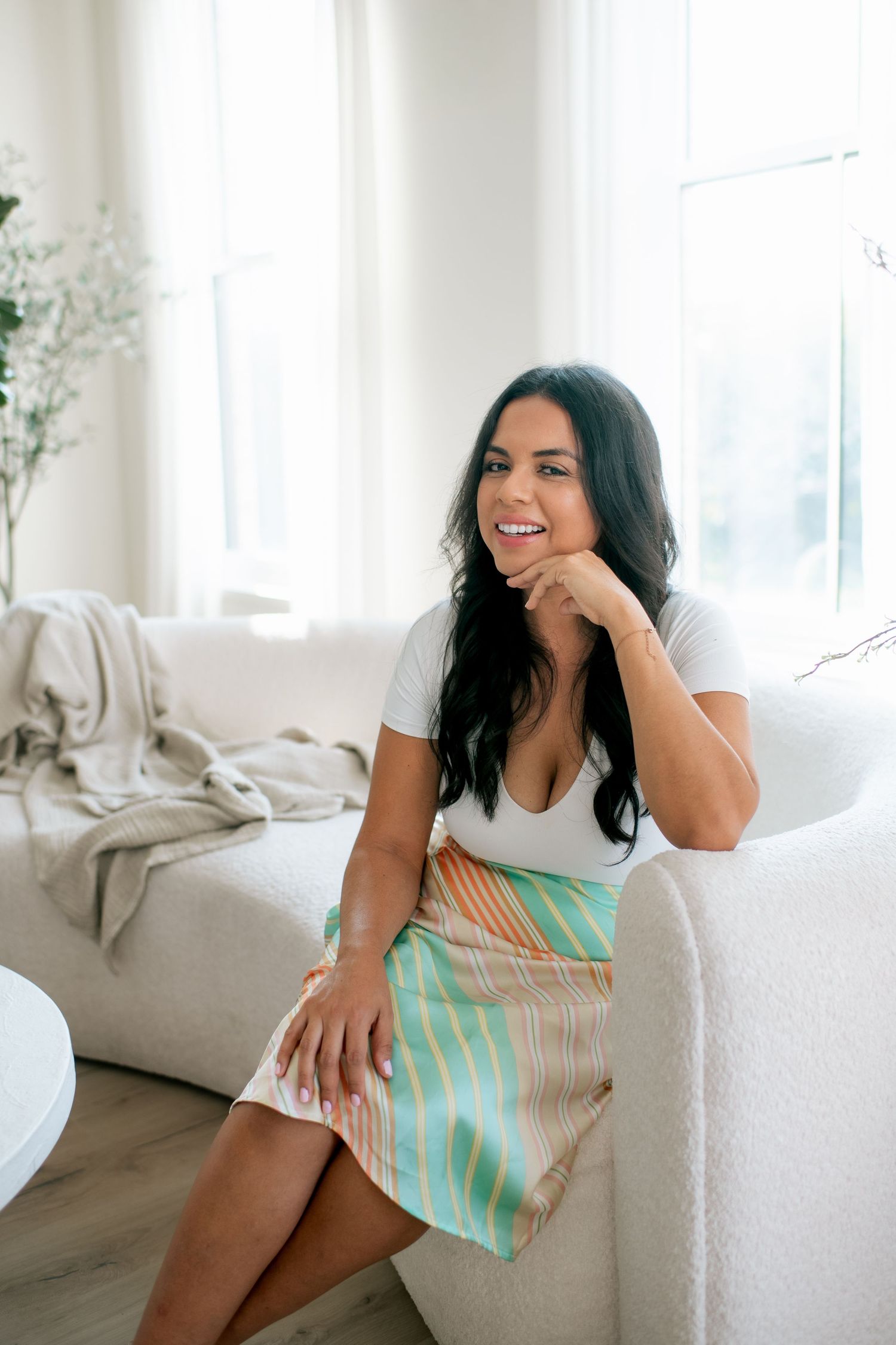 A joyful person relaxes on a white couch in a bright, airy room wearing a mint green and white patterned dress.