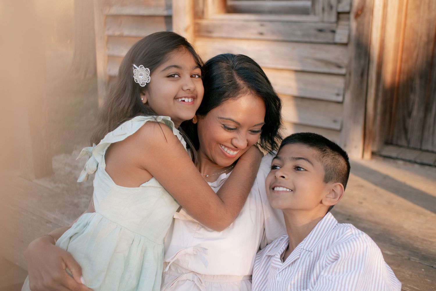 Three family members share a tender moment together while posing outdoors in warm evening lighting.