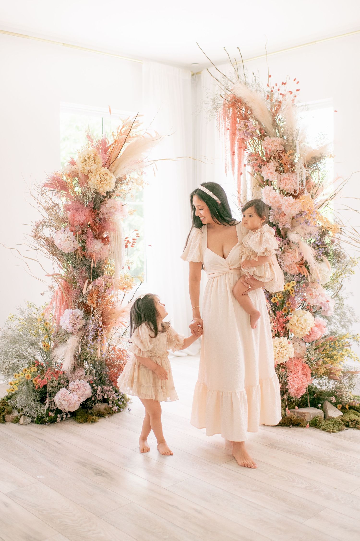 Elegant floral display with pink and cream blooms frames an intimate moment against white walls and light wood floors.
