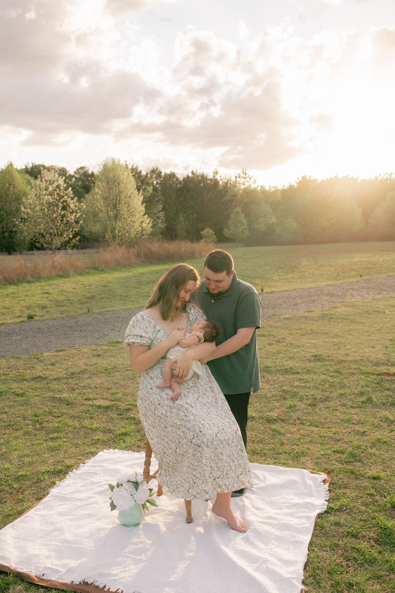 Family picnic scene on white blanket in grassy field during sunset.