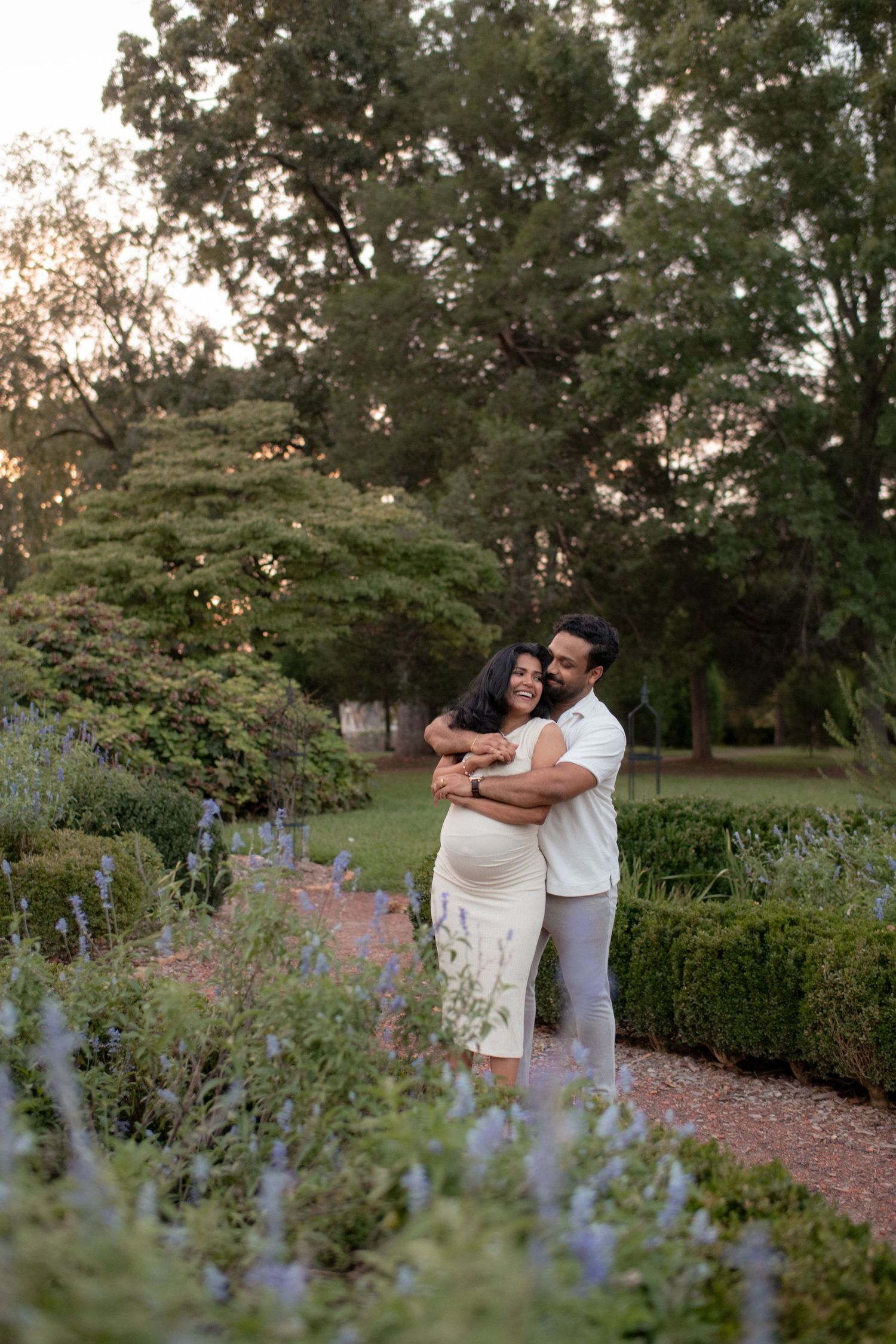 Couple shares intimate moment among purple flowers in garden setting during golden hour.