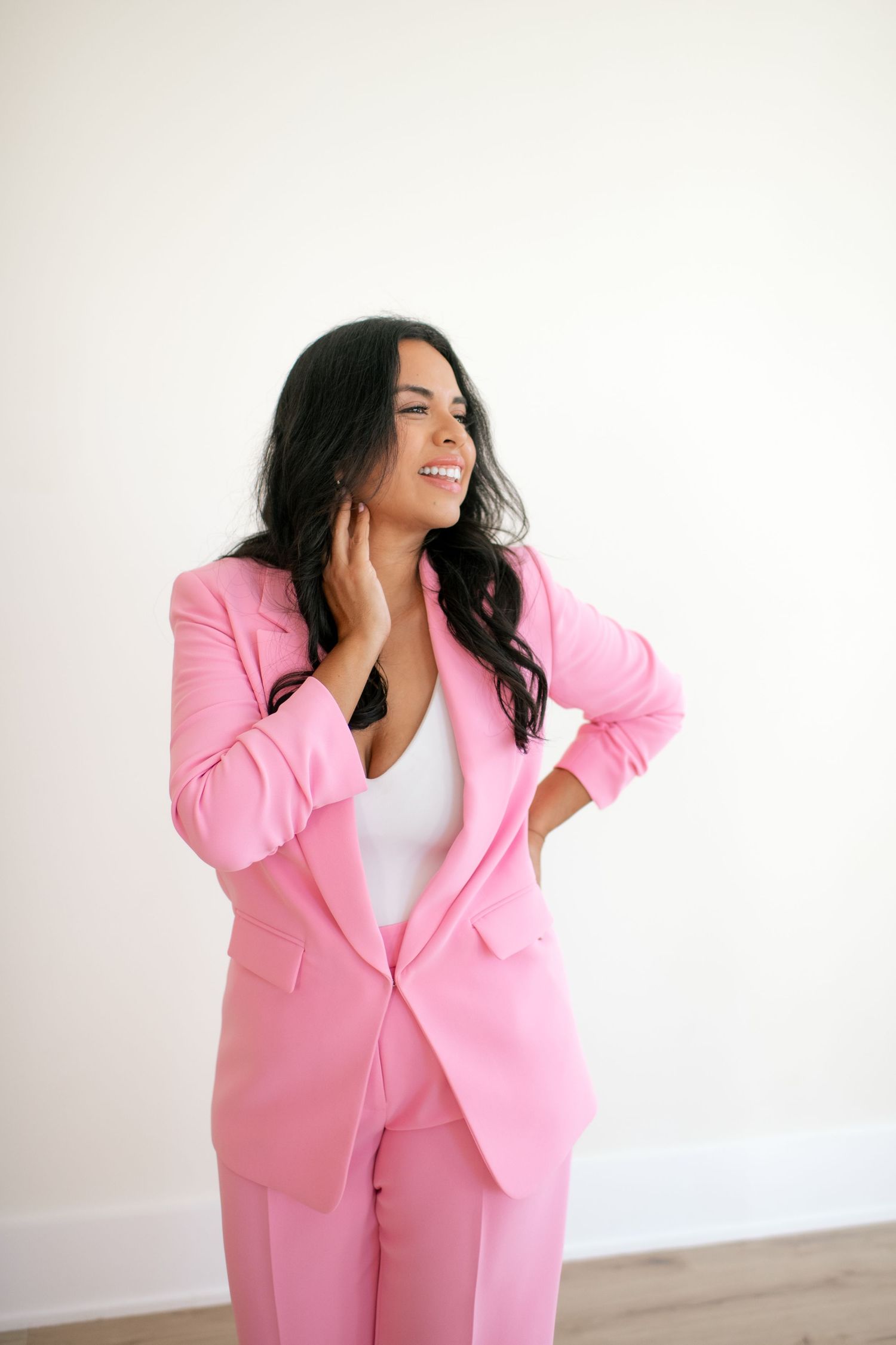 Professional photoshoot featuring a bright pink business suit against a white background.