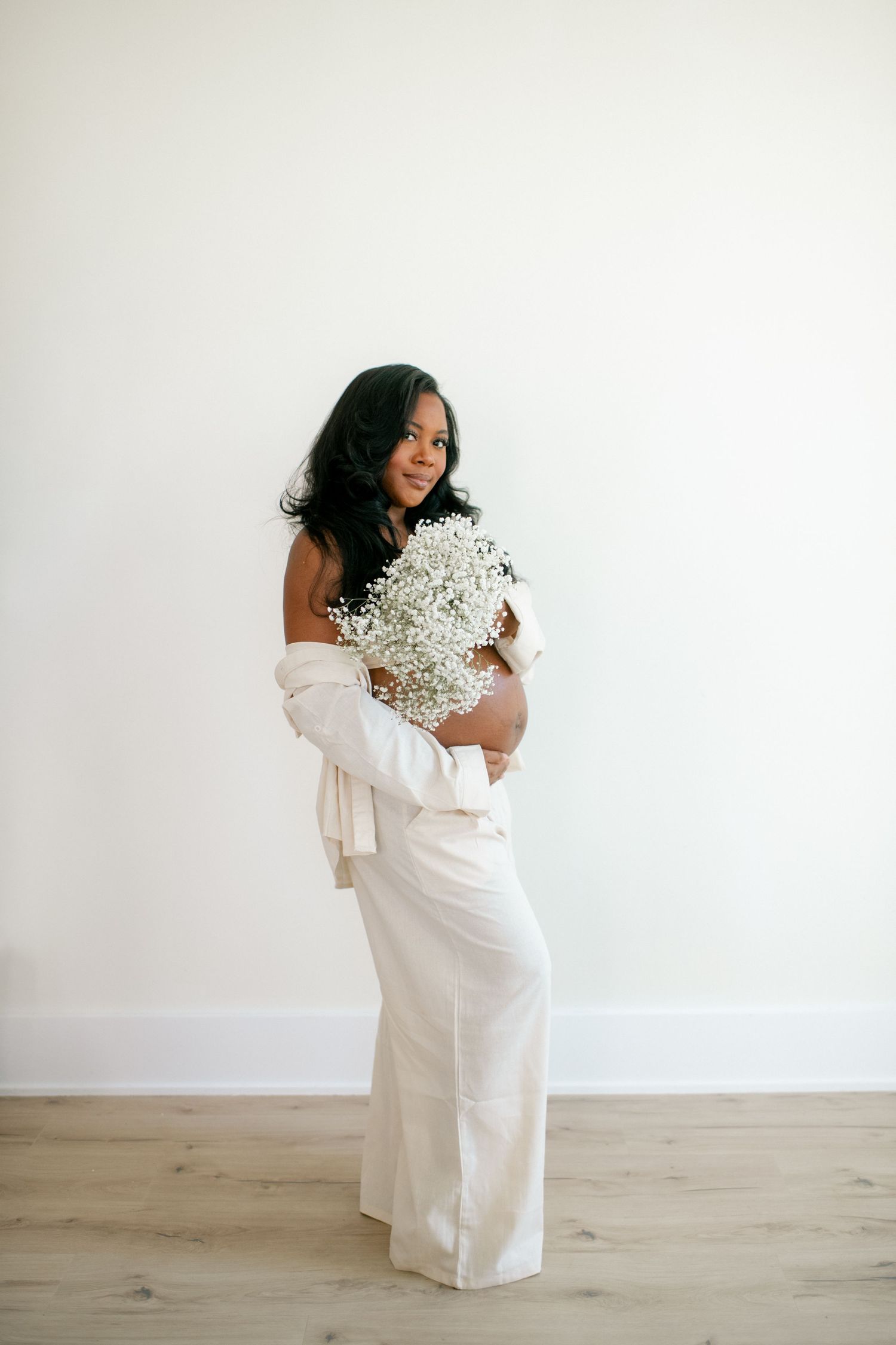 Modern maternity photography with minimalist white backdrop and baby's breath flower accents.