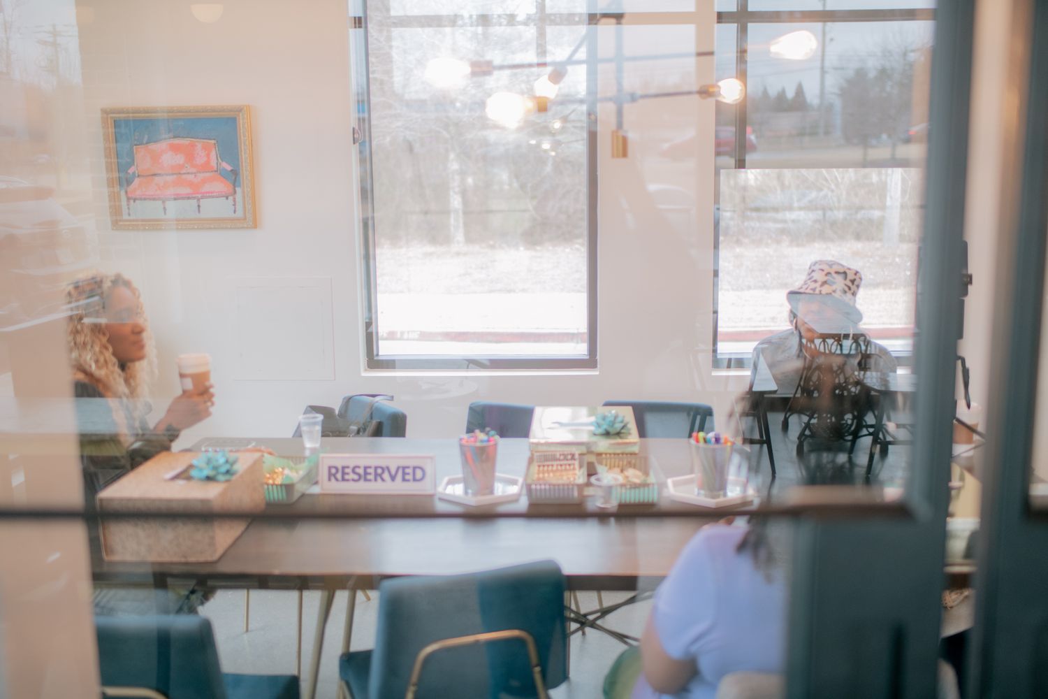 A bright meeting room with windows shows multiple people seated at tables reviewing materials.