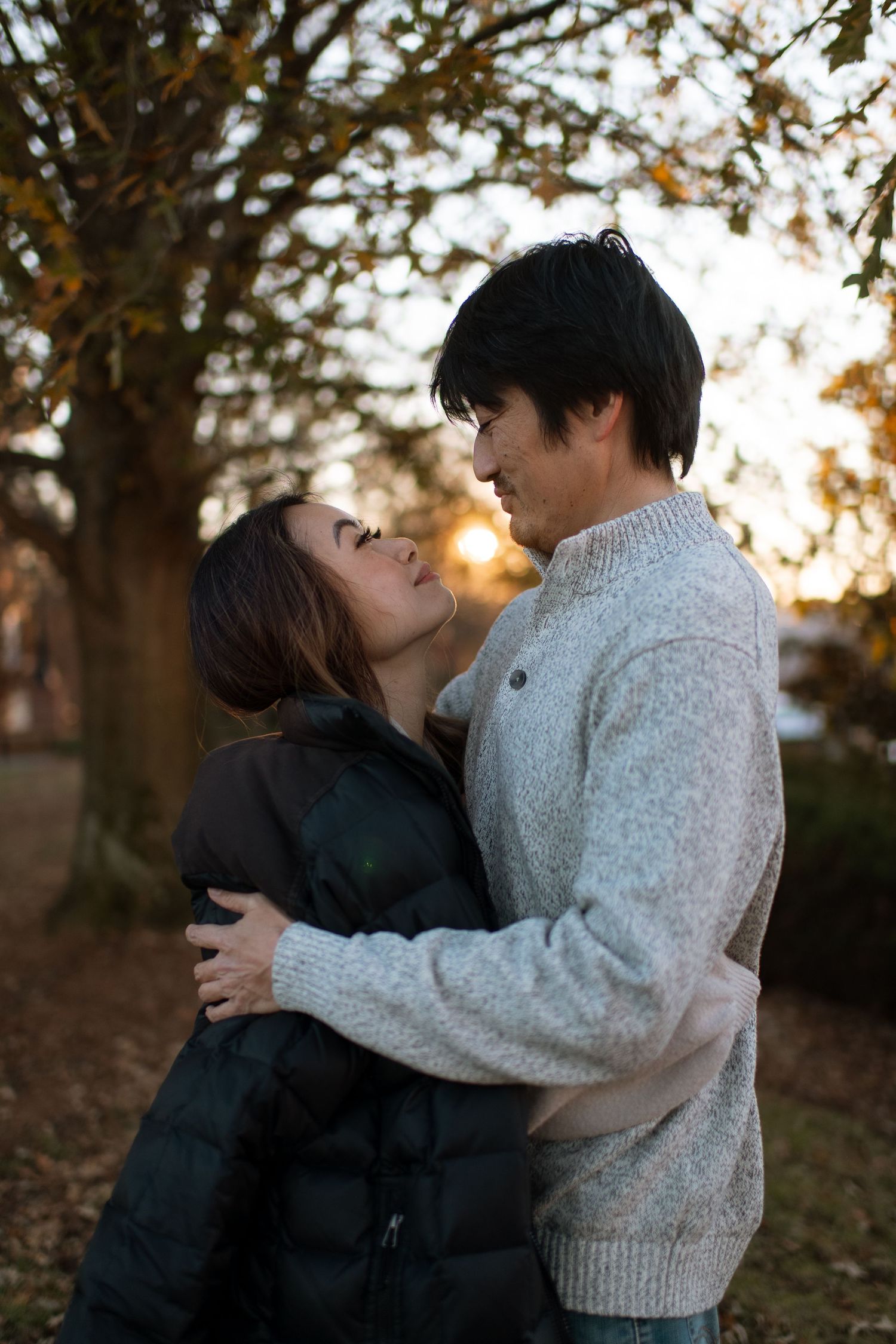 Couple in warm sweaters sharing intimate moment among autumn trees at sunset.
