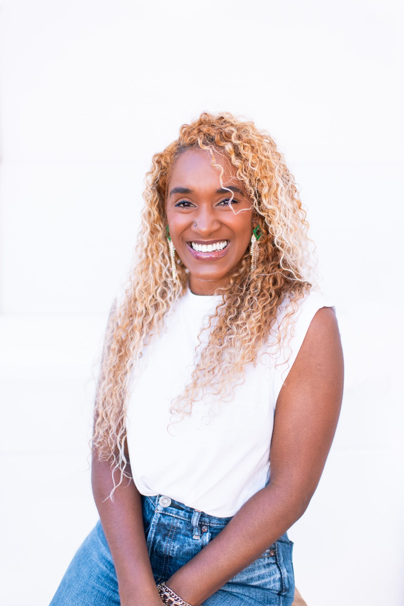 Person in white sleeveless top and denim smiles against white background.