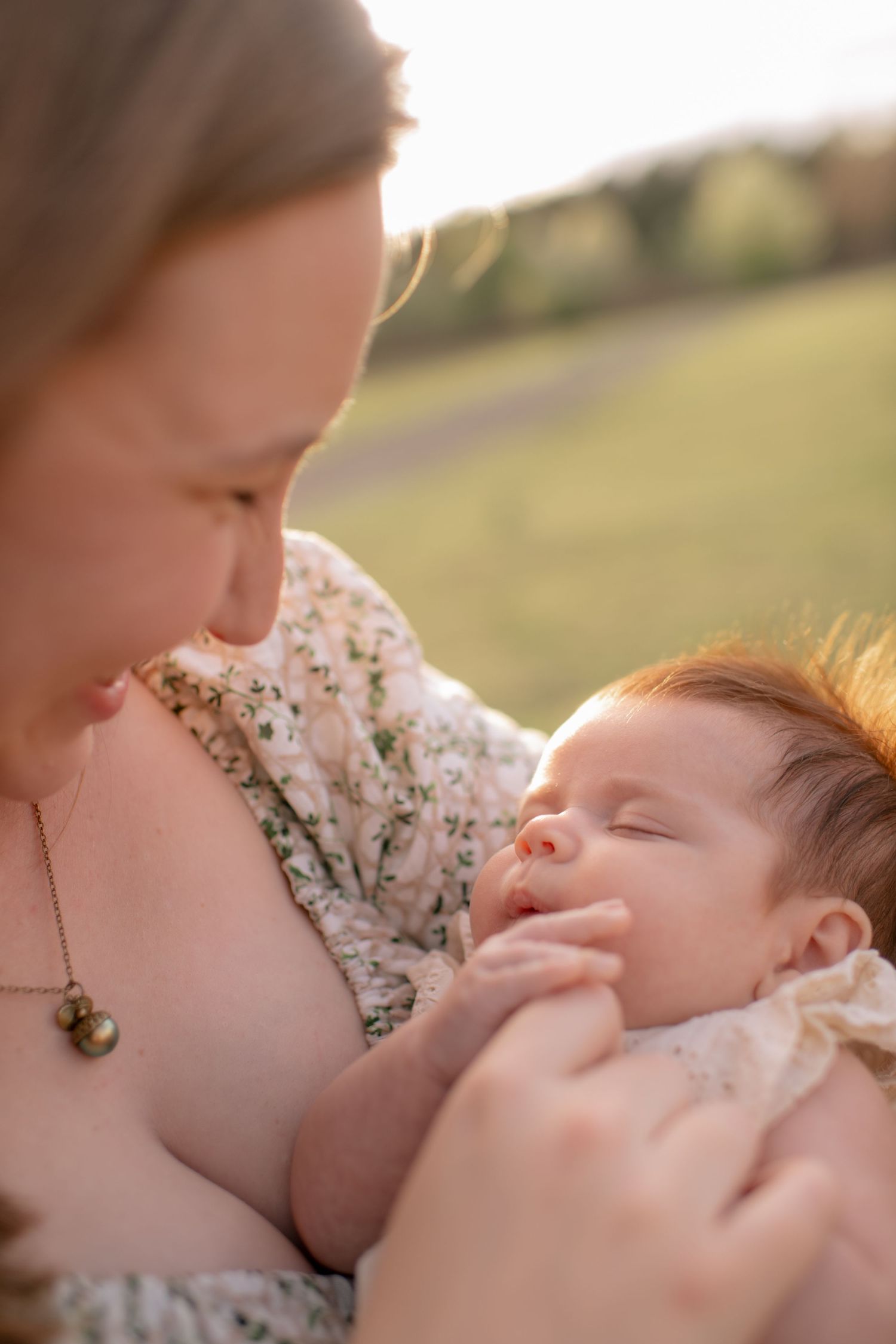 A tender moment between parent and sleeping baby in warm sunlight with floral dress and necklace details.