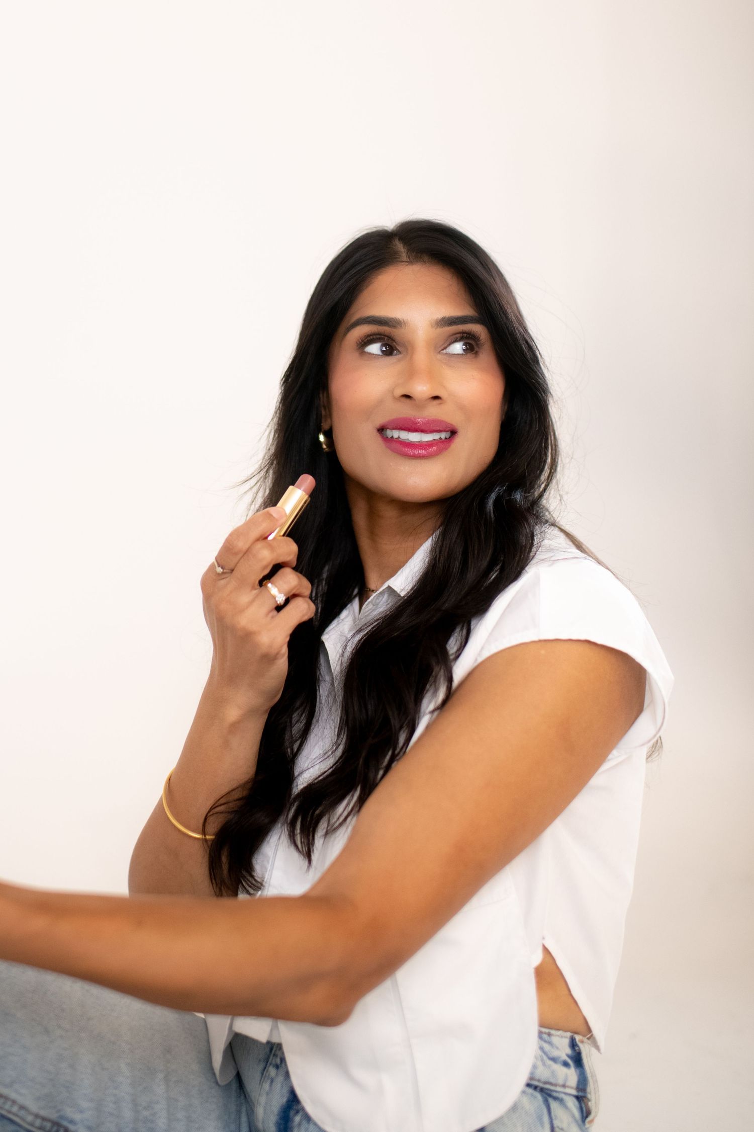 Person in white top and jeans poses playfully against white background in studio setting.