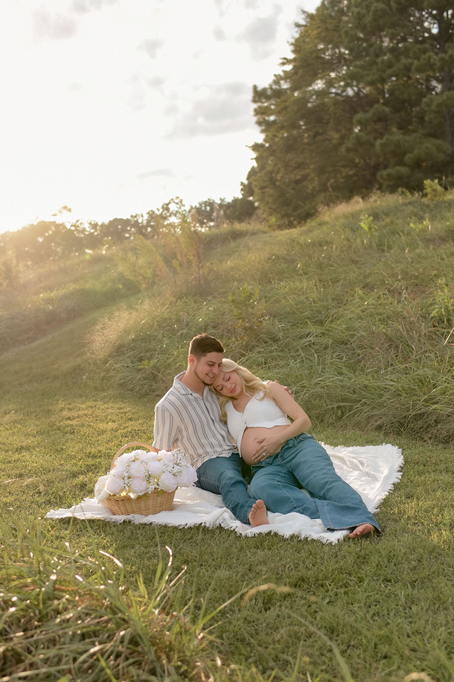 Couple lying on white blanket in sunlit grassy field during golden hour.