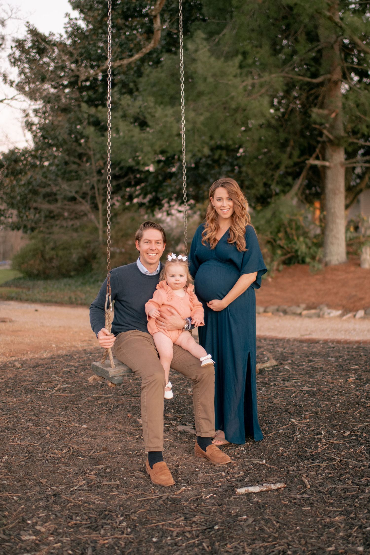 Family poses together near a swing set in an outdoor setting during sunset.