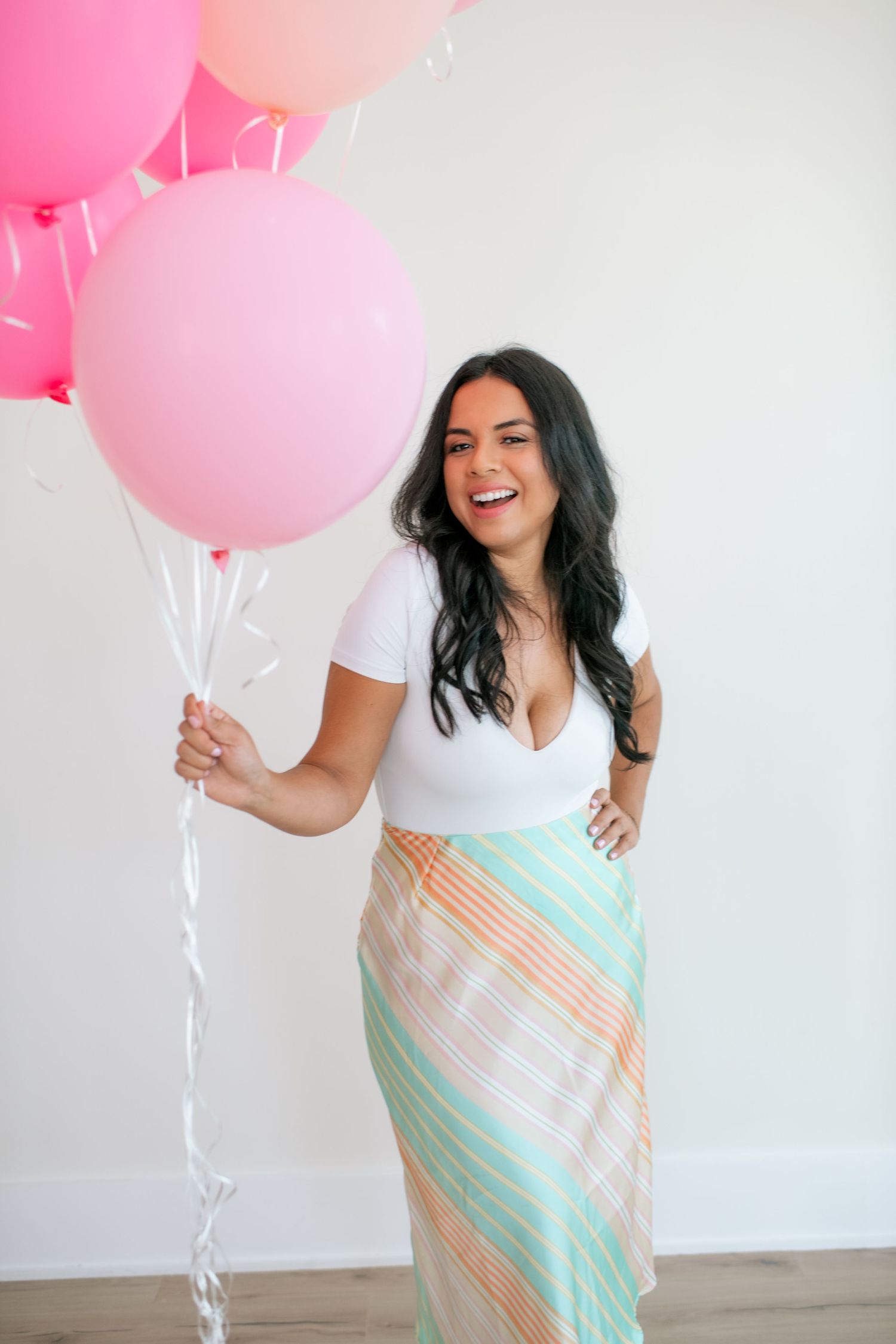 Person in striped dress poses with pink balloons against white background.