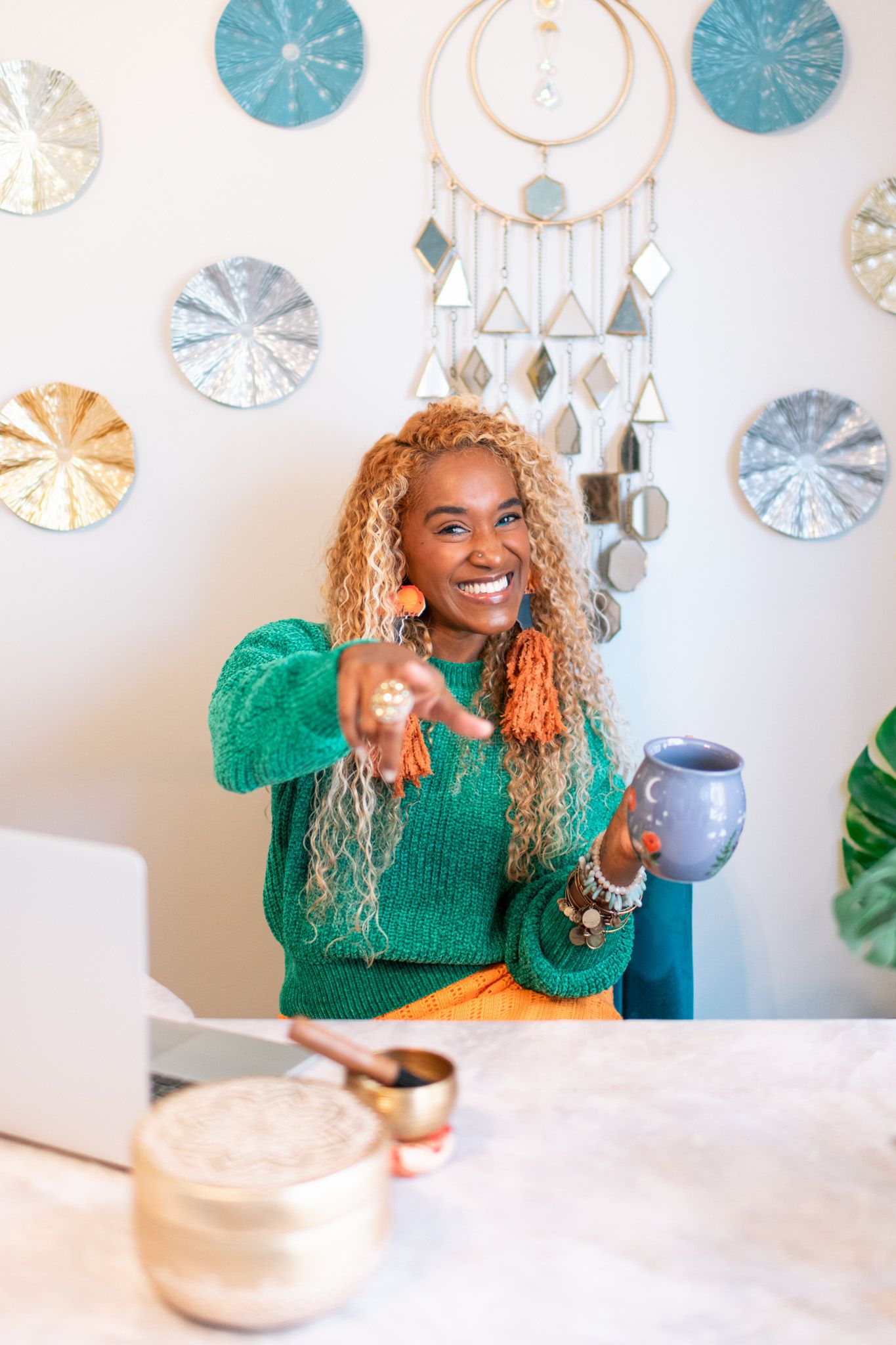 Person in emerald green sweater laughs while seated at table with blue wall decor.